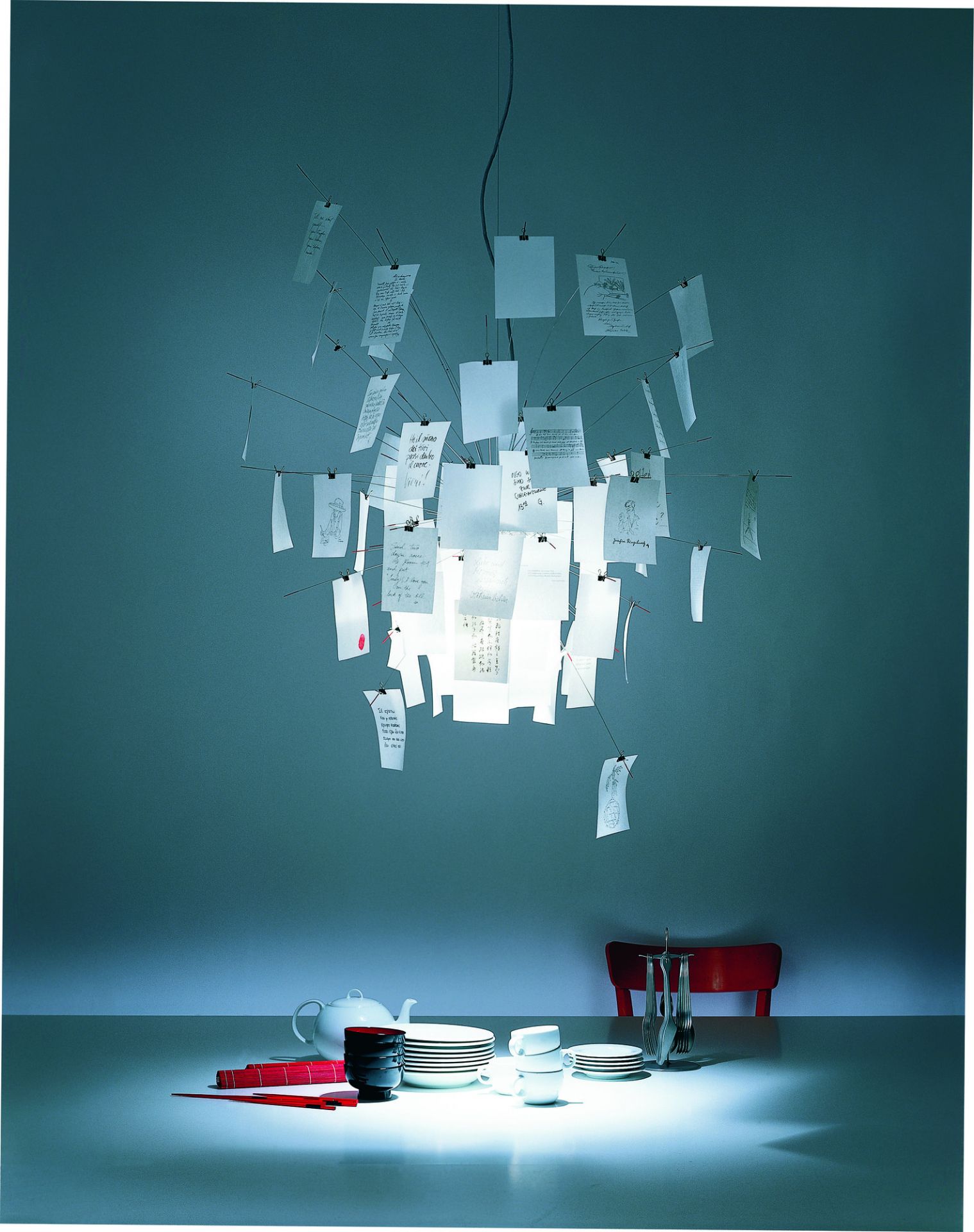 Zettel'z Hängeleuchte von Ingo Maurer über Esstisch mit Geschirr, moderne Designerlampe mit Notizen.