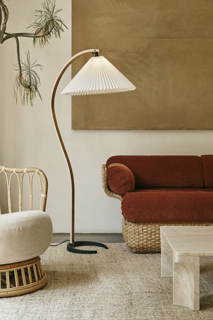 Gubi Timberline Stehleuchte im Wohnzimmer mit Rattansessel, braunem Sofa und beigem Teppich.