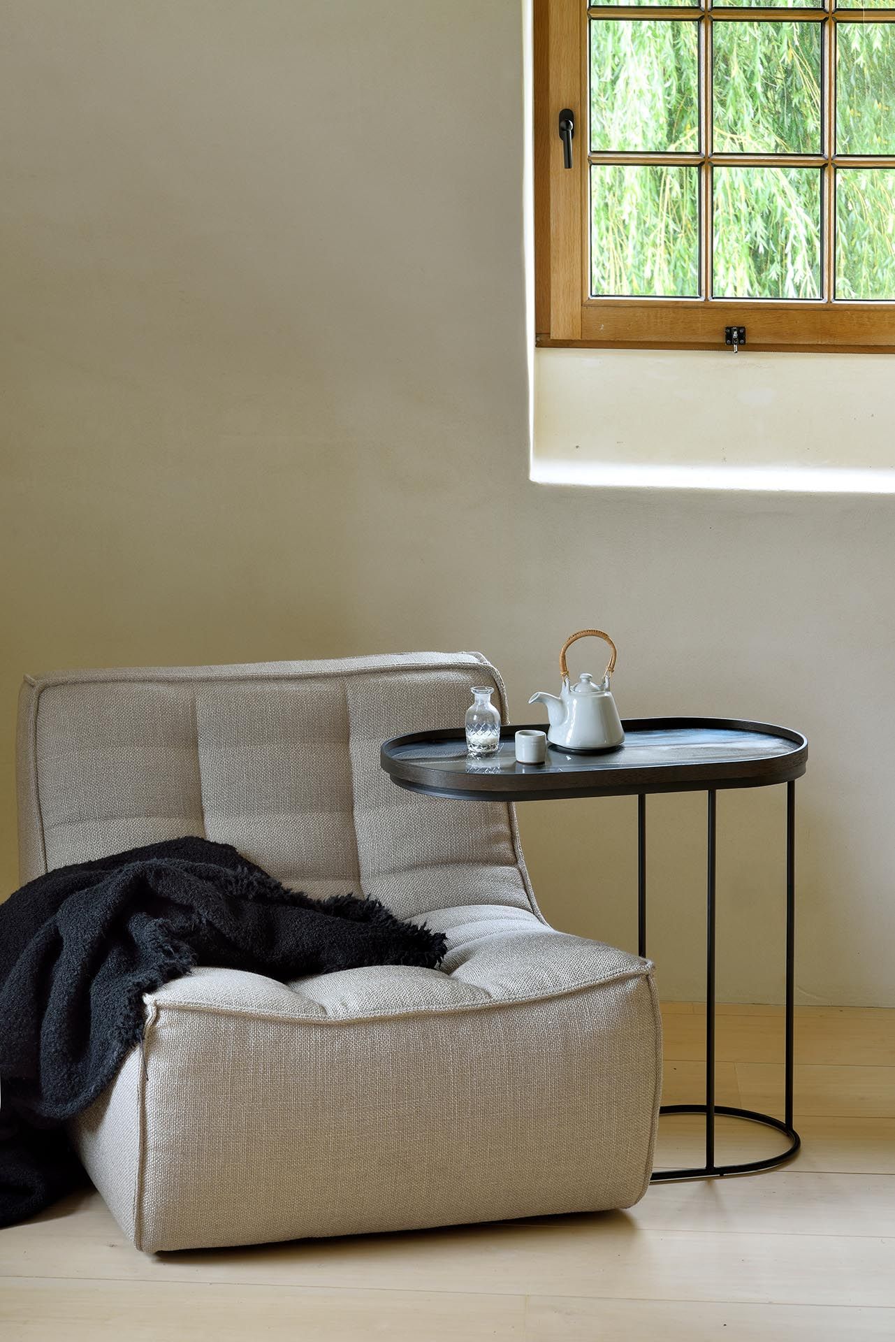 Ethnicraft Beistelltisch aus Holz, schwarz lackiert, neben Sessel mit Teekanne und Glas.