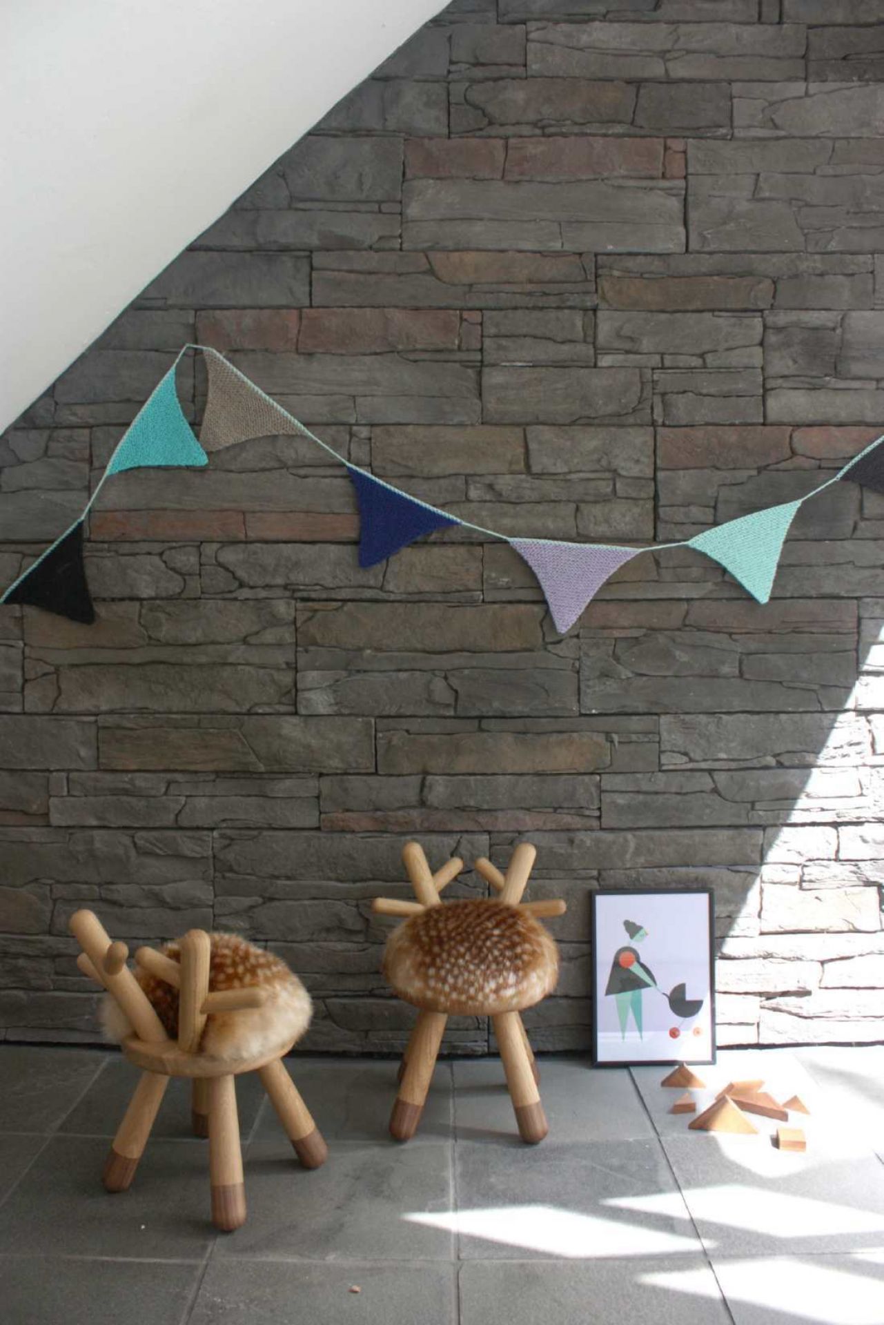 Zwei Bambi Chair Kinderstühle von EO  vor einer Steinwand mit Wimpelkette und Spielzeug.