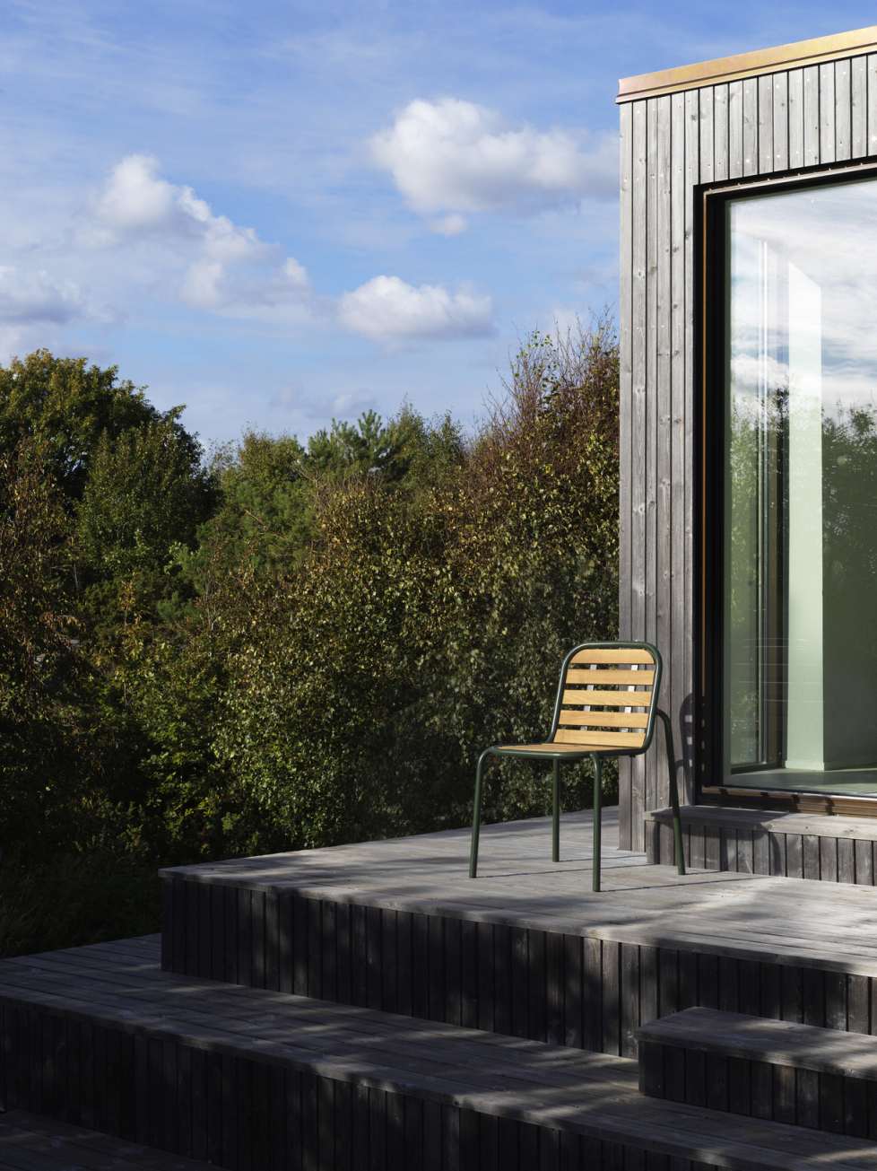 Vig Chair Wood Stuhl von Normann Copenhagen auf Holzterrasse vor modernem Holzhaus.