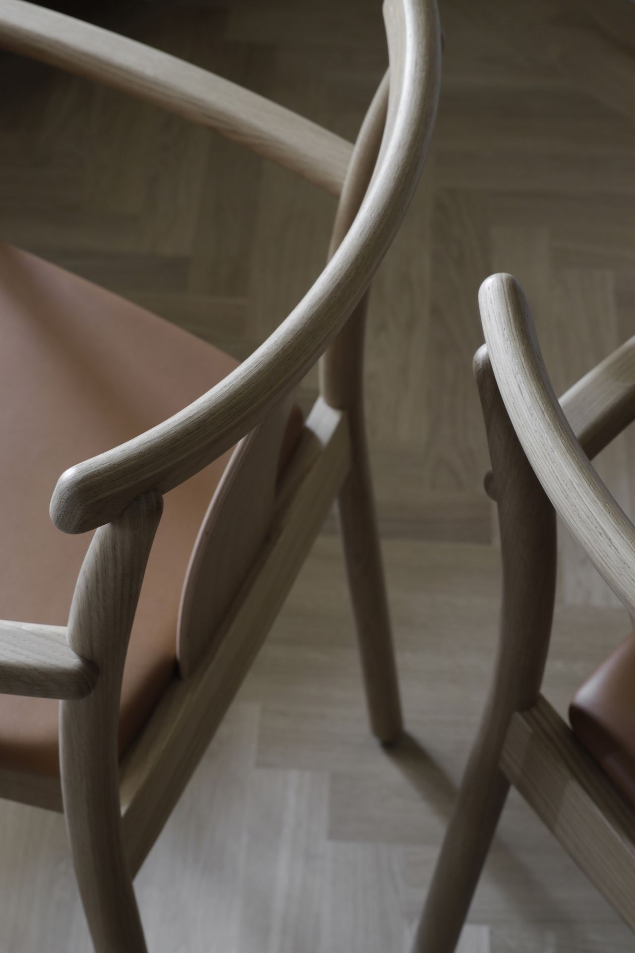 Detailaufnahme von zwei Merkur Dining Chair Stühlen mit Armlehnen von Audo Copenhagen, Holzgestell und Ledersitz.