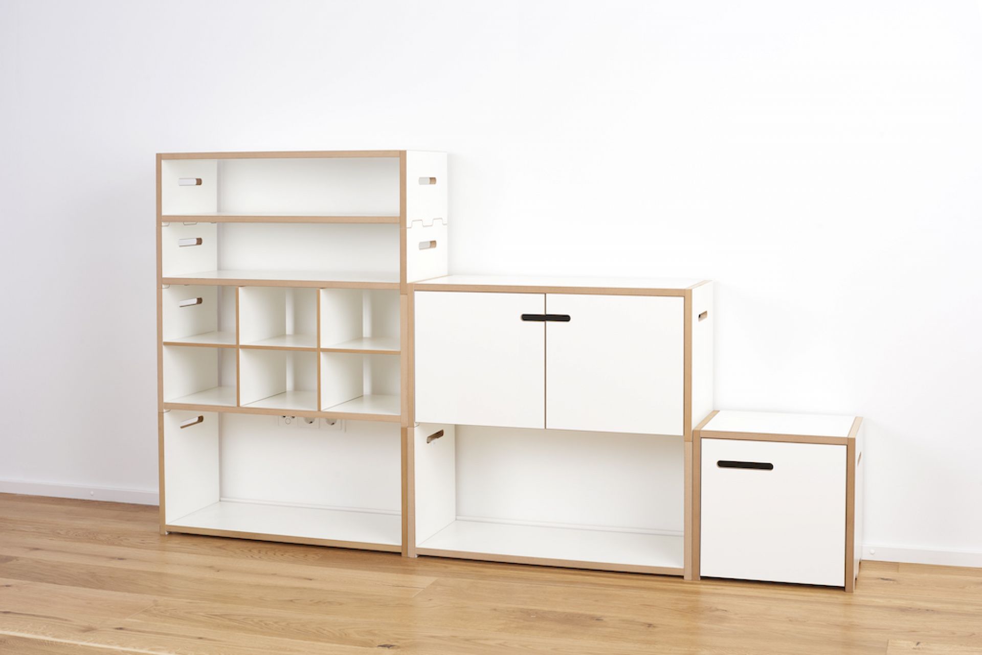 Tojo Halbstark Regalsystem: Weißes, modulares Regal mit Fächern, Schrankelementen und Schublade auf hellem Holzboden.
