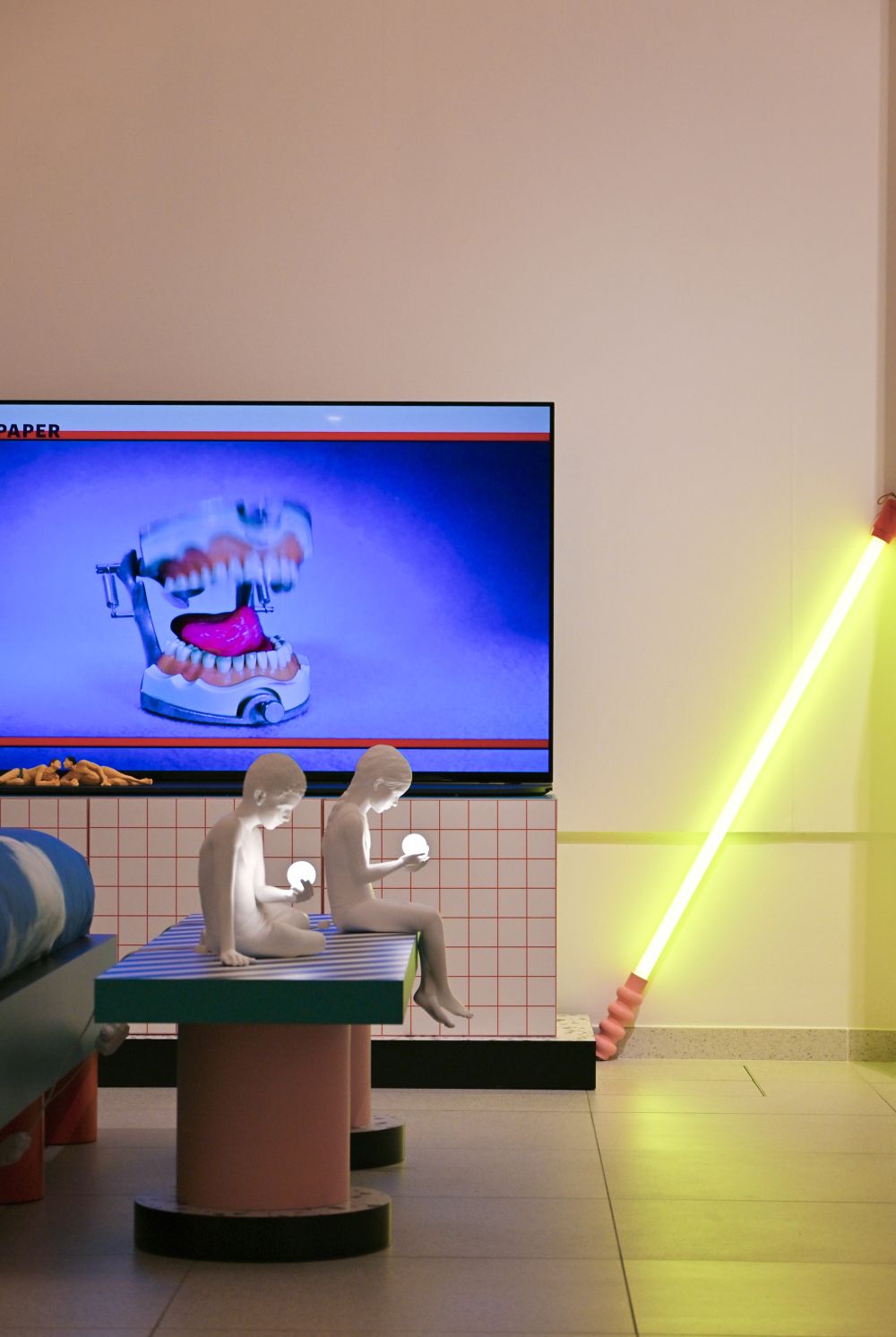 Superbench Bank Seletti: Bunte Designerbank mit zwei Skulpturen, die leuchtende Kugeln halten, vor einem Fernseher.