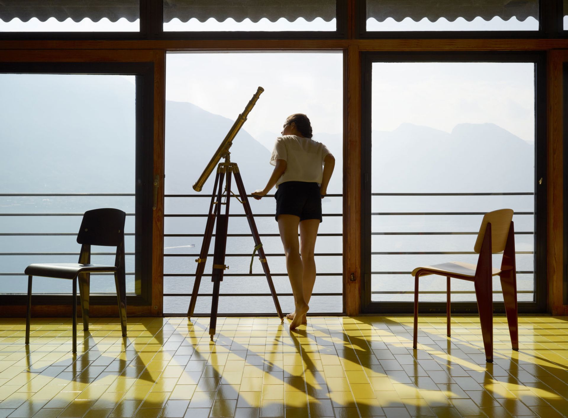 Vitra Standard Stuhl in Szene gesetzt mit Teleskop und Frau vor Panoramafenster mit Seeblick.