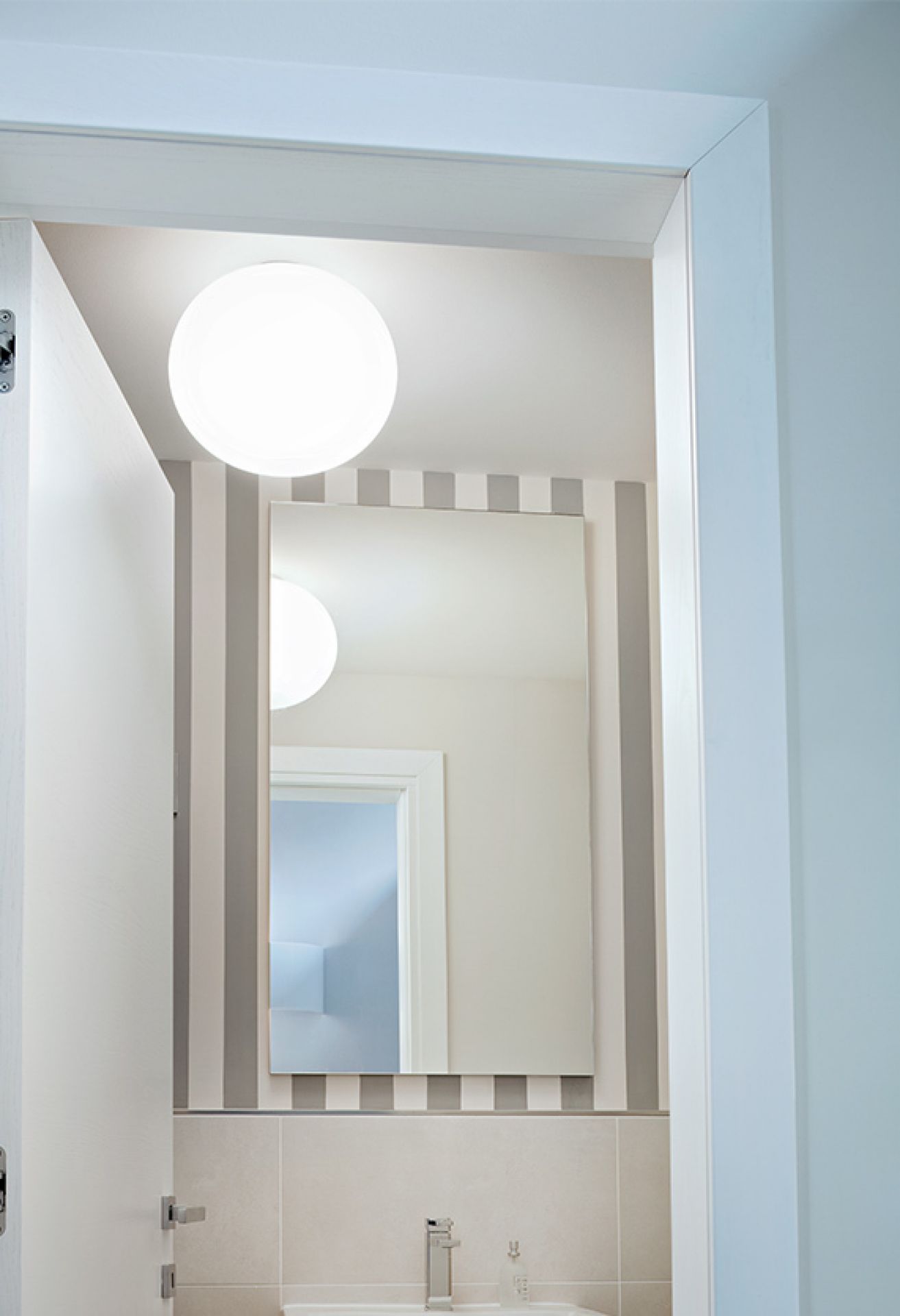 Glo Ball Deckenleuchte von Flos: Runde, weiße Lampe im Badezimmer mit Spiegel und Streifenmuster.