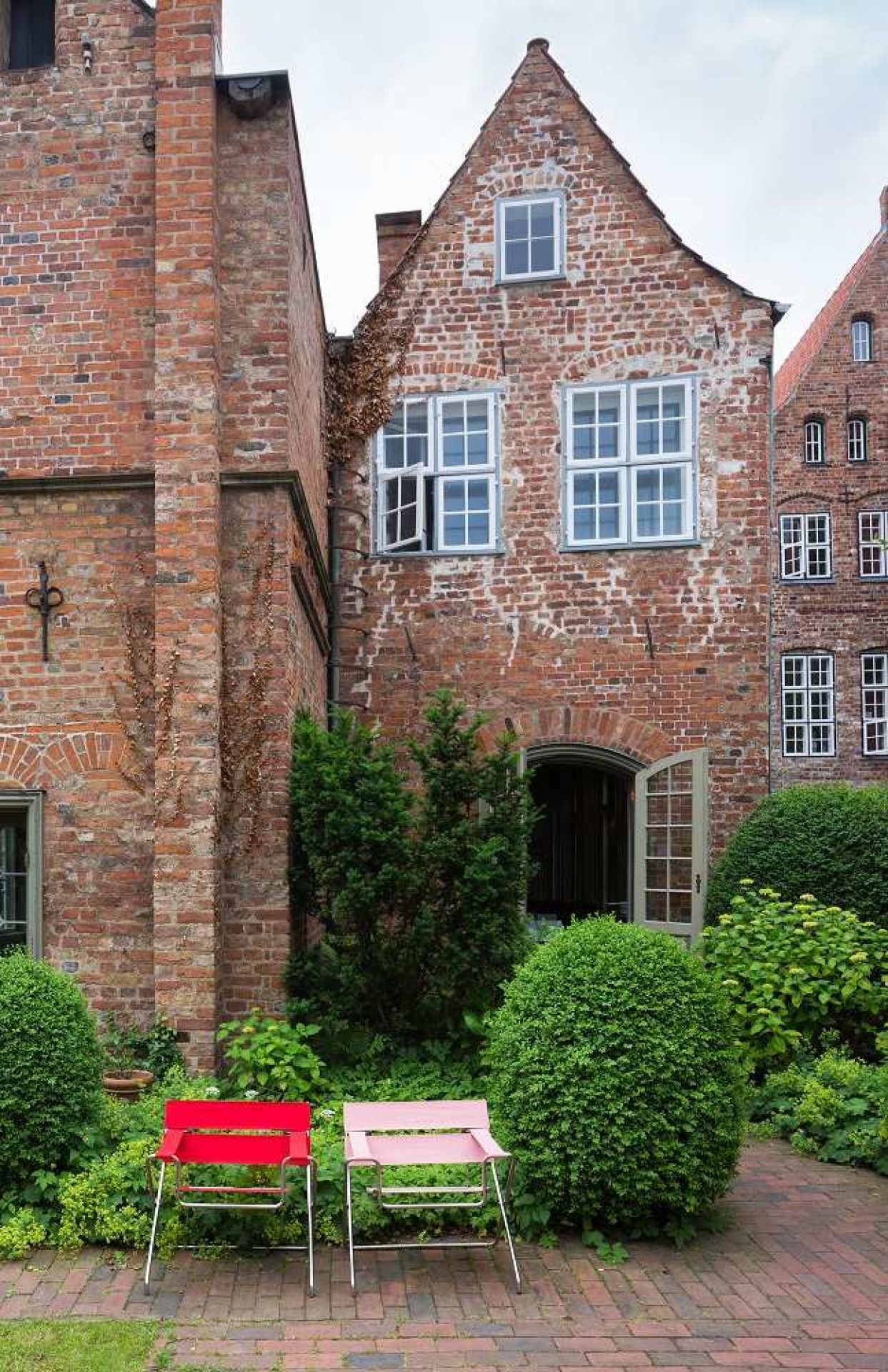 Zwei D4 Bauhaus Faltsessel Tecta in Rot und Rosa vor Backsteingebäude und Grünanlage.