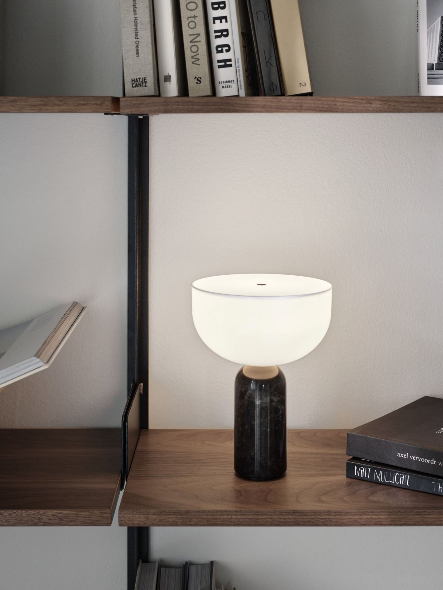 Schwarze Kizu Tischleuchte von New Works auf Holzregal, modernes Design, stimmungsvolle Beleuchtung.