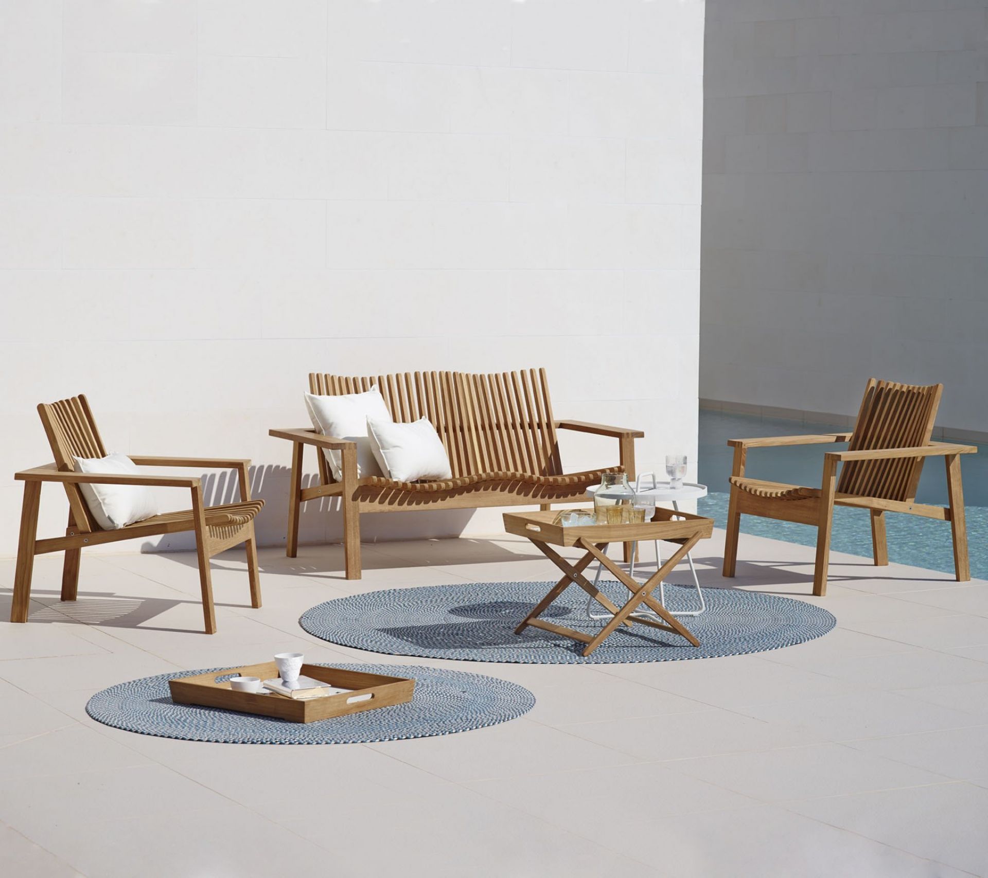 Amaze Outdoor Loungesessel von Cane-Line aus Teakholz mit Kissen und Beistelltischen auf Teppichen.