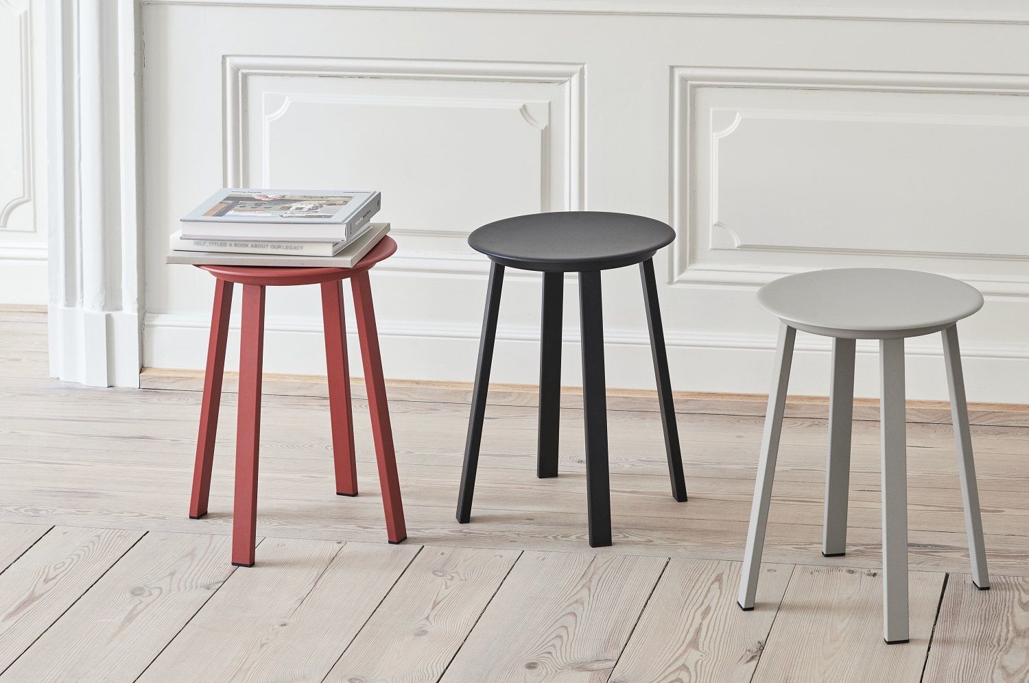 Drei Hay Revolver Stool Hocker in Rot, Schwarz und Grau vor weißer Wand auf Holzboden.