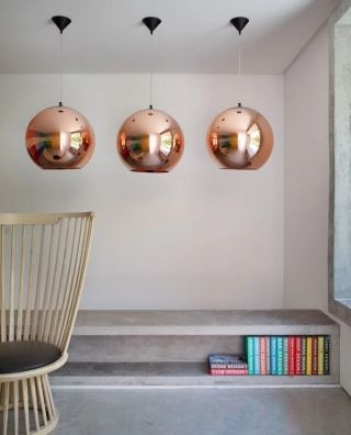 Drei moderne, runde Pendelleuchten aus Kupfer hängen über einer Treppe mit Büchern im Wohnzimmer.