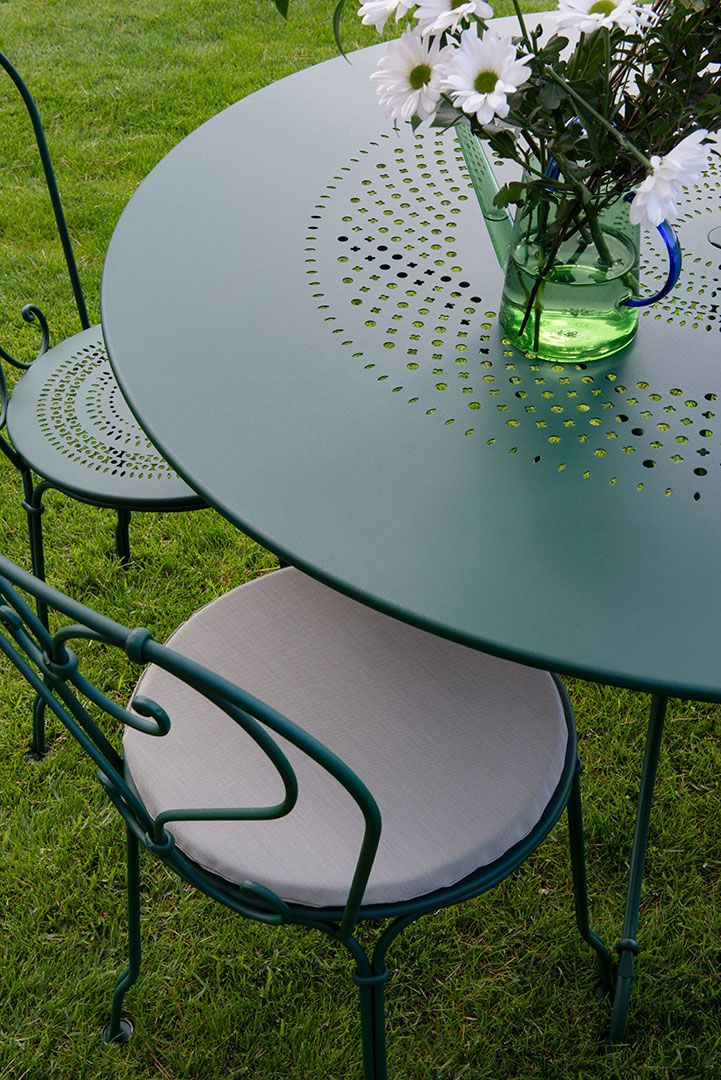 Grüner Fermob 1900 Gartentisch Ø 117 cm mit Stuhl und Blumenvase auf Rasen.