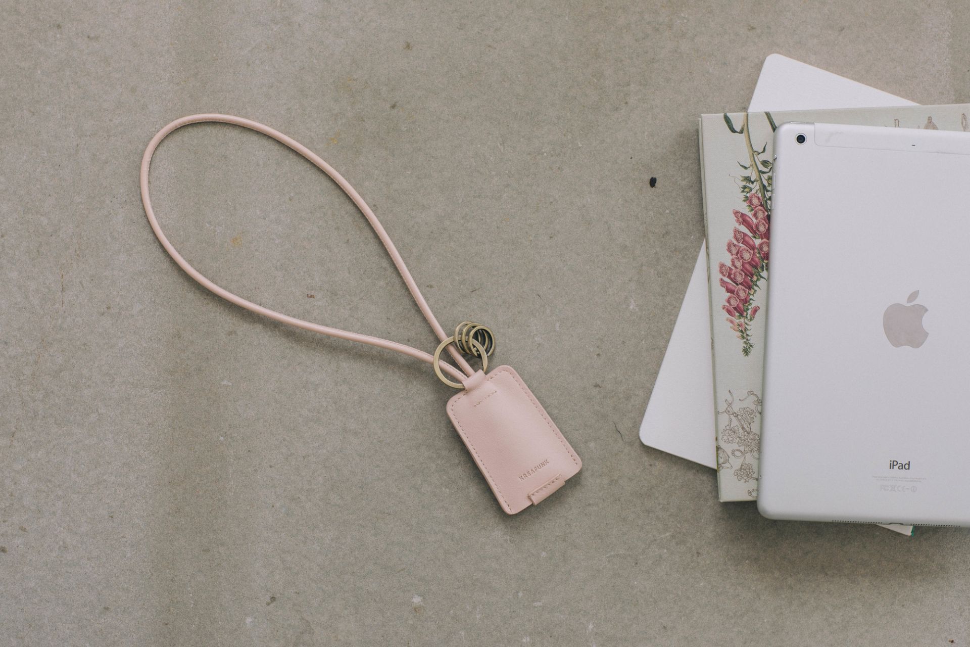 Nahaufnahme des Kreafunk cCHAIN Schlüsselanhängers in Rosa mit USB-Kabel, neben einem iPad.