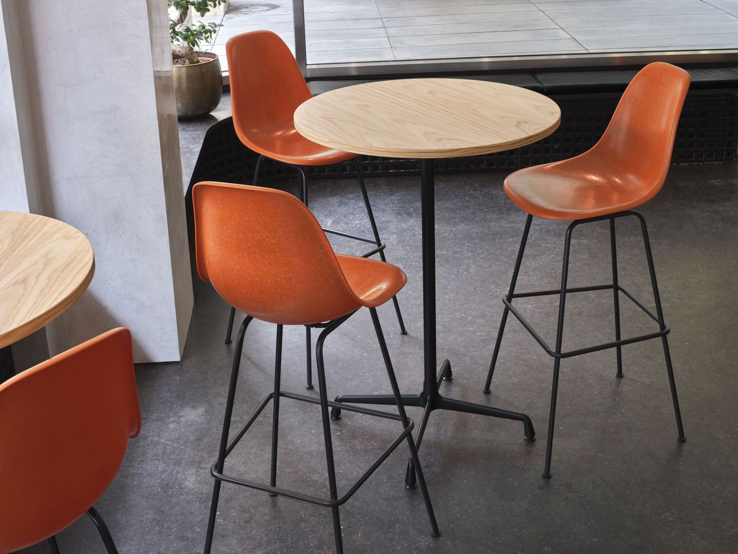 Eames Fiberglass Bar Stool High von Vitra, orangefarbene Barhocker mit schwarzem Gestell an Holztisch.