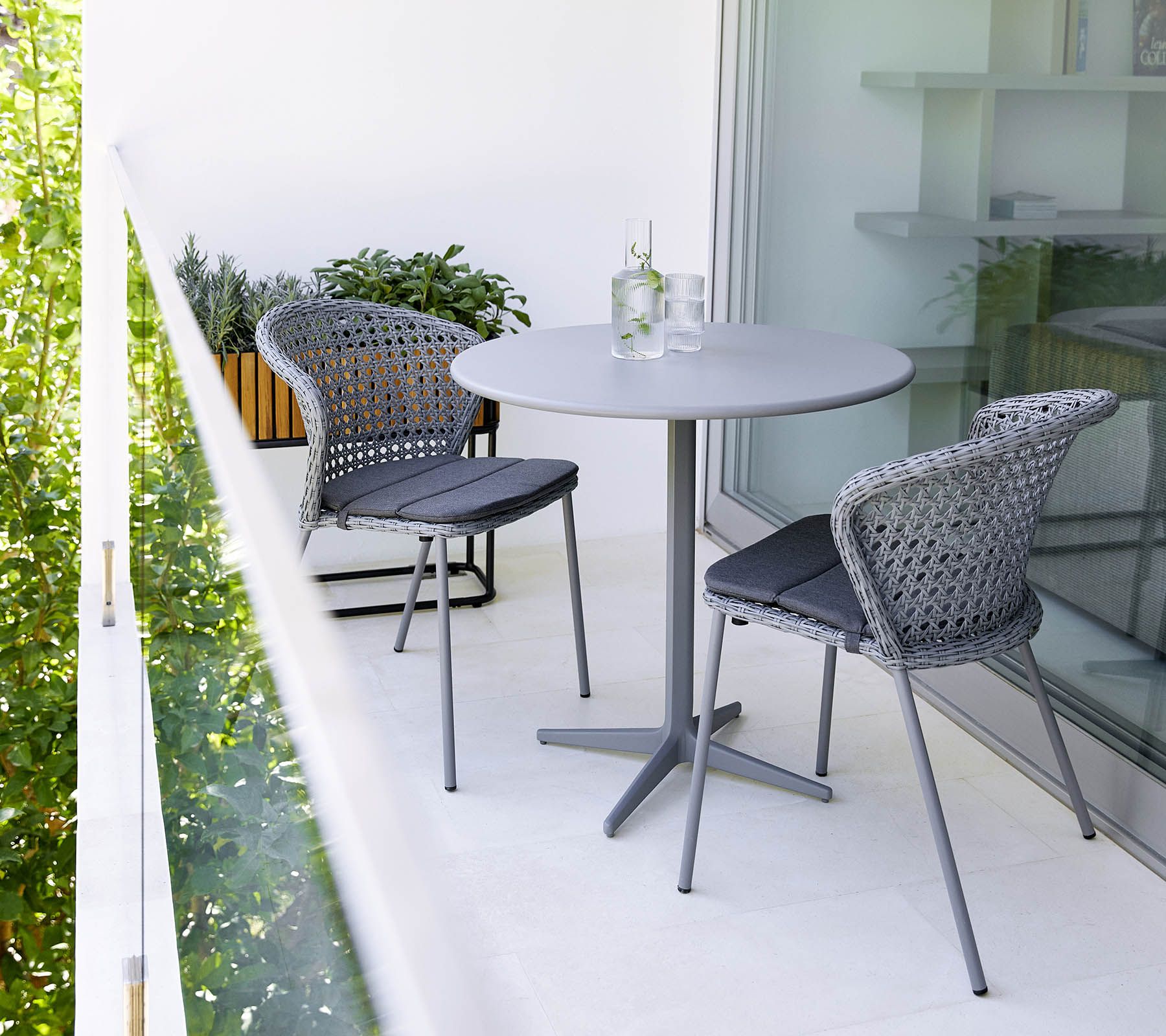 Graue Lean Stühle von Cane-Line mit Rattan-Geflecht und passendem Tisch auf einem Balkon.