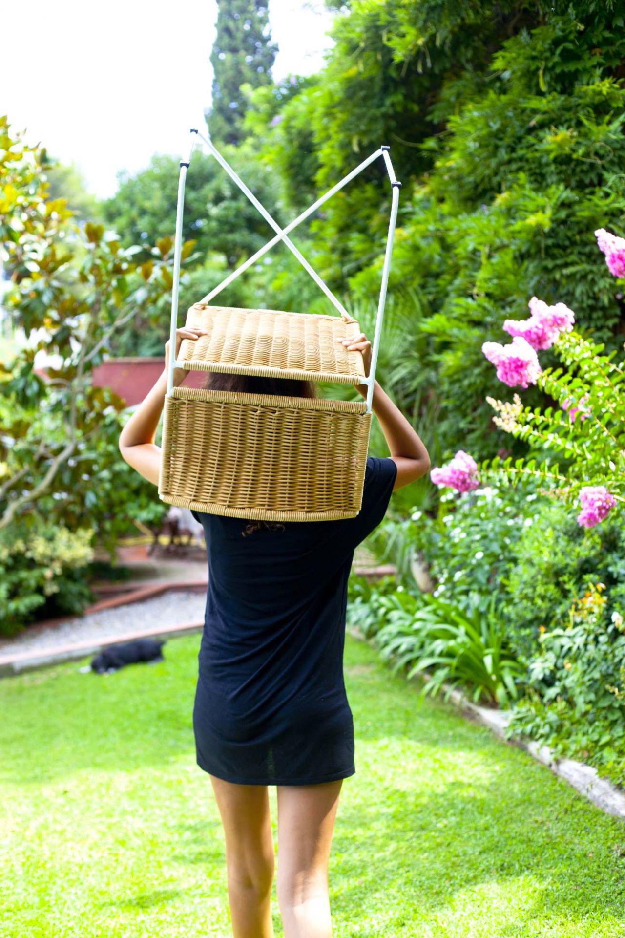 Frau trägt Ramón Rattanstuhl von Santa & Cole im Garten. Rattanmöbel und Gartendesign.