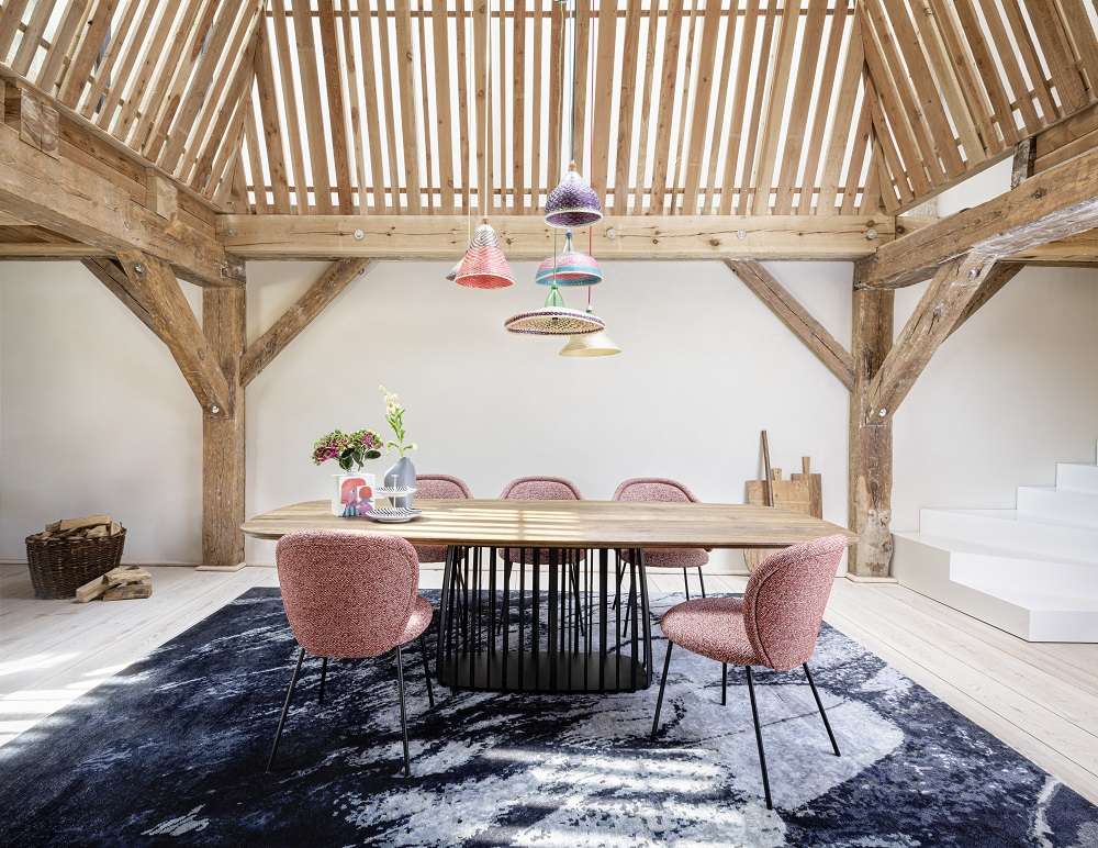 Esszimmer mit Ona Stühlen der Freifrau Manufaktur, Holztisch, Design-Teppich und dekorativen Lampen.