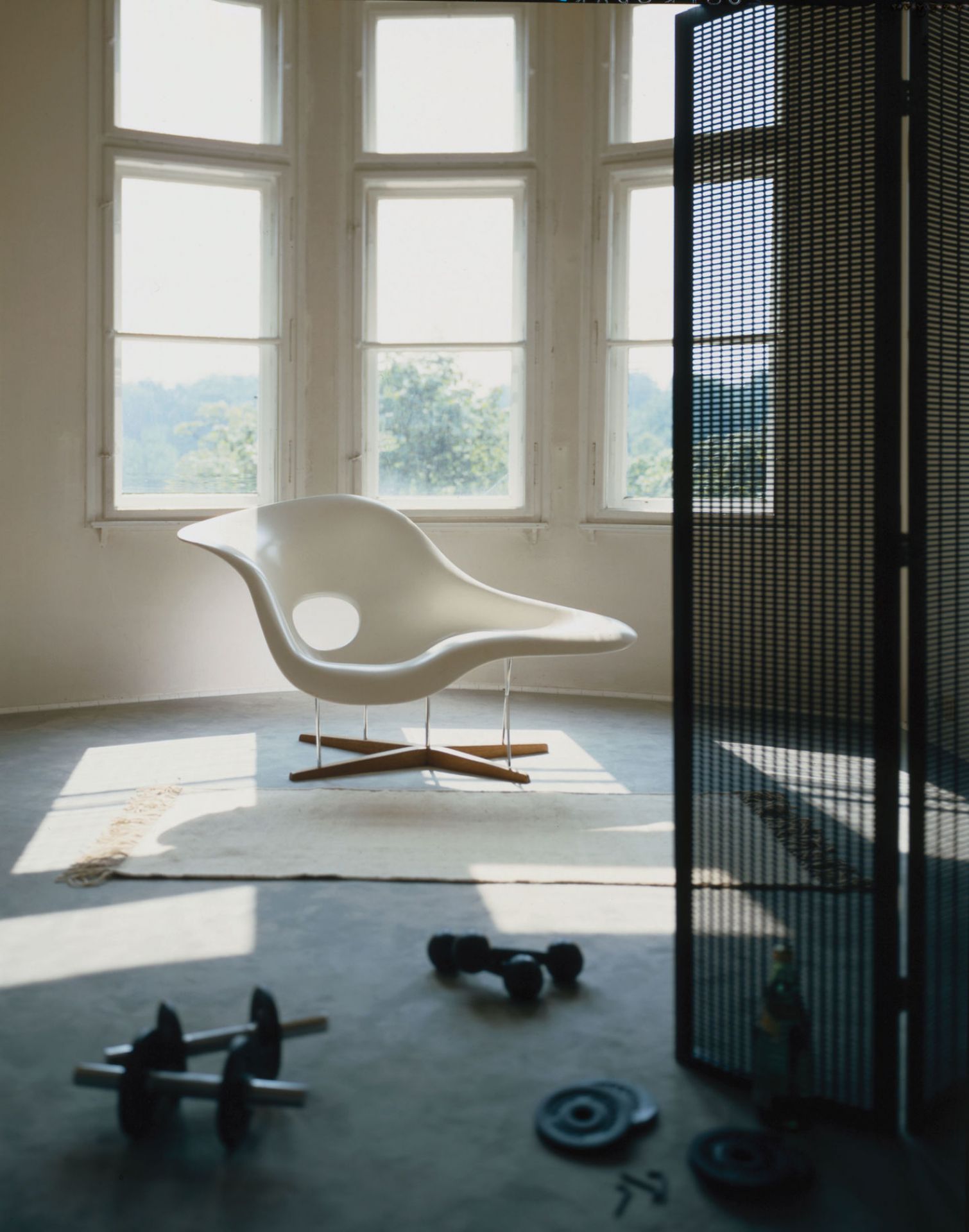 Vitra La Chaise Liege in weißem Kunststoff auf Holzkreuzfuß vor Fenster und Raumteiler.