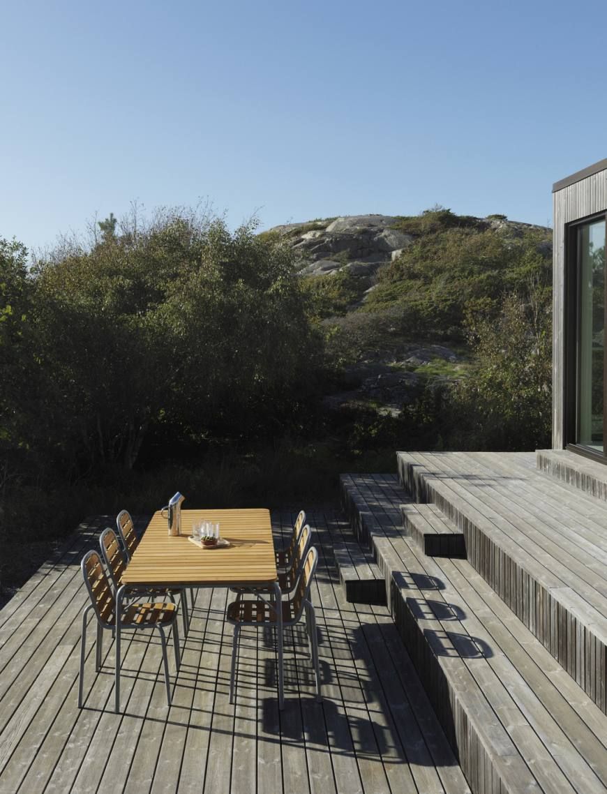 Normann Copenhagen Vig Table Outdoor auf einer Holzterrasse mit Stühlen und Blick auf die Natur.