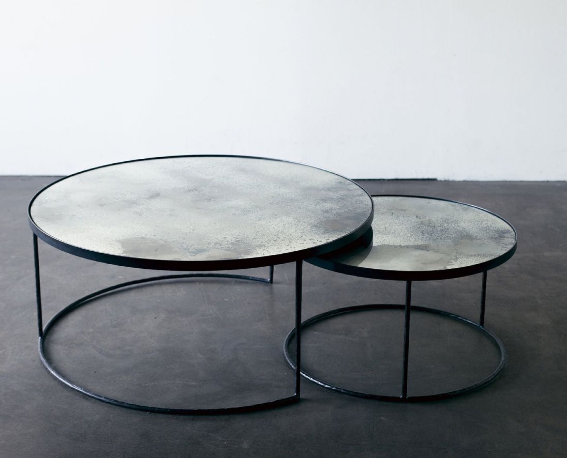 Ethnicraft Couchtisch Set: Zwei runde Beistelltische mit Spiegelglasplatte und schwarzem Metallgestell.
