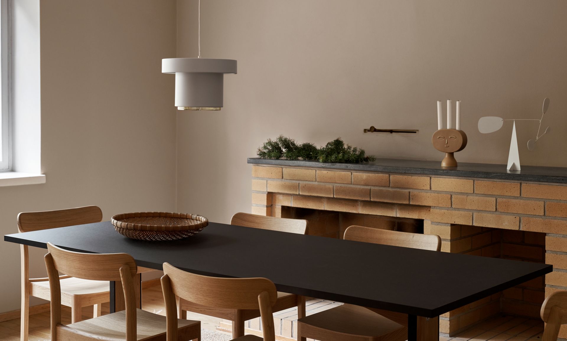 A201 Pendelleuchte von Artek über Esstisch mit Holzstühlen und Kamin im Hintergrund.
