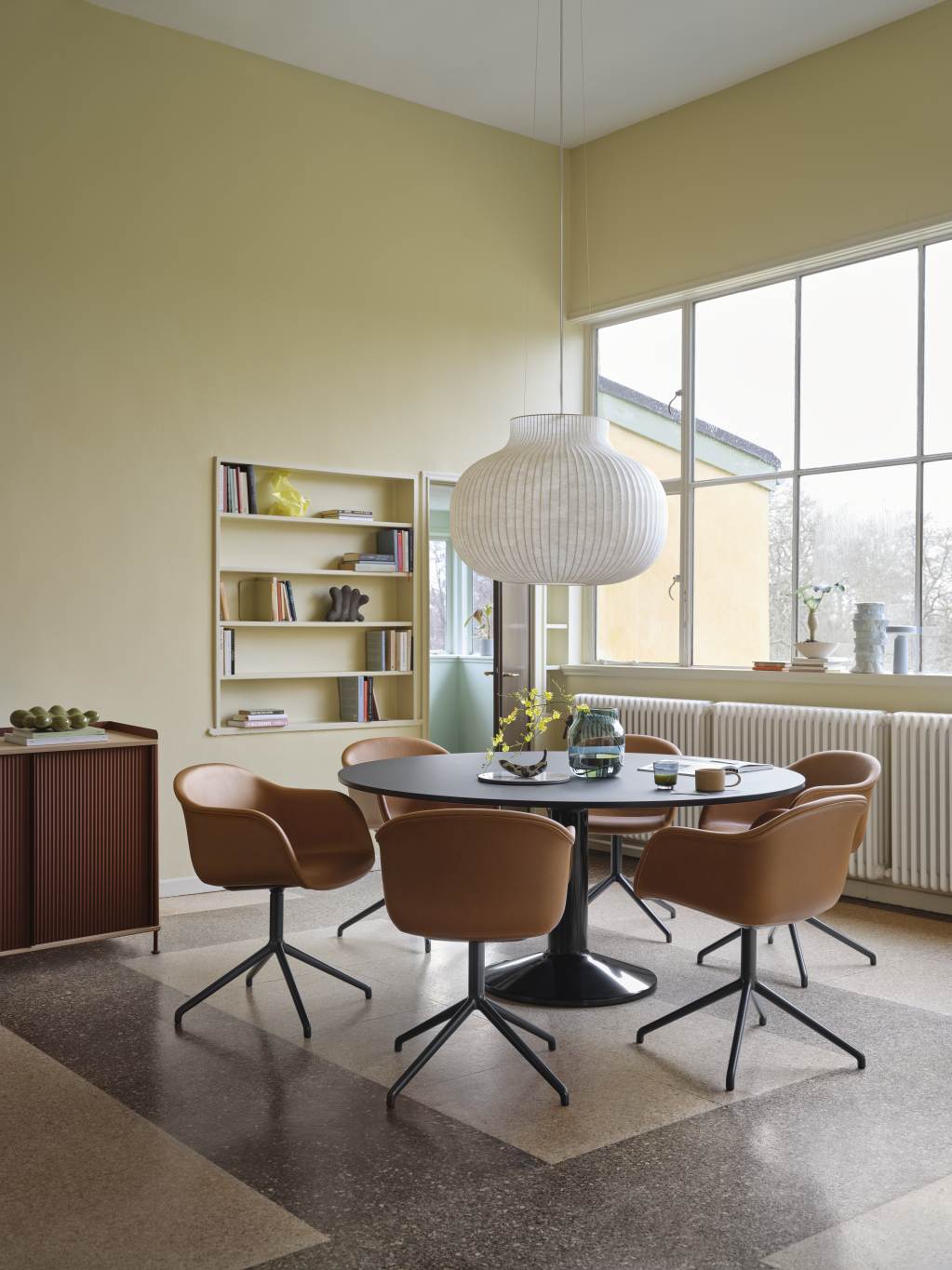 Muuto MIDST Table Esstisch mit runder, schwarzer Tischplatte und braunen Stühlen in einem hellen Esszimmer.