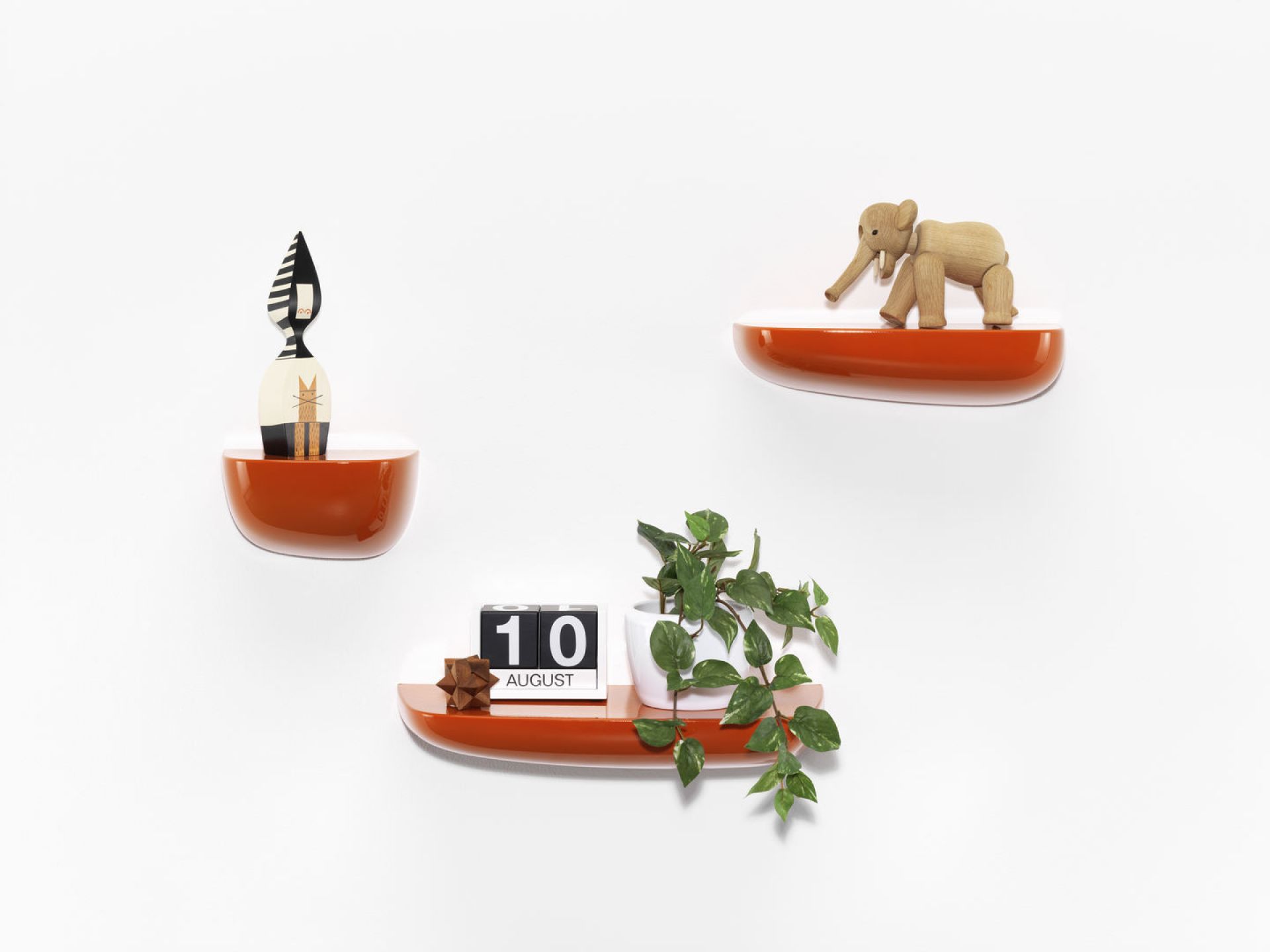 Orangefarbene Vitra Corniches Wandboards in verschiedenen Höhen mit Dekoration an einer weißen Wand.