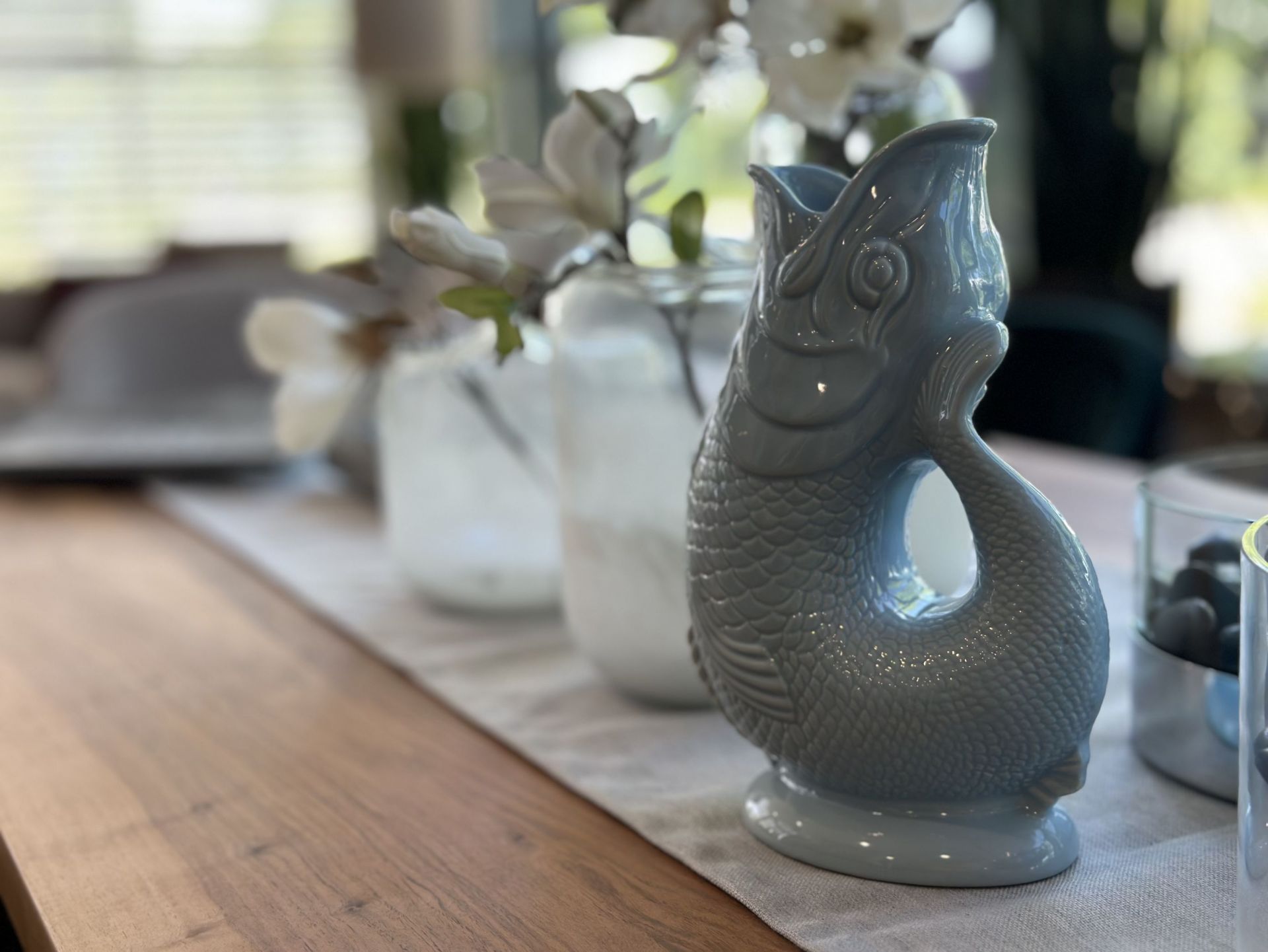 Helle Gluckigluck Karaffe in Fischform, hellblau, XL, als Vase auf einem Tisch.