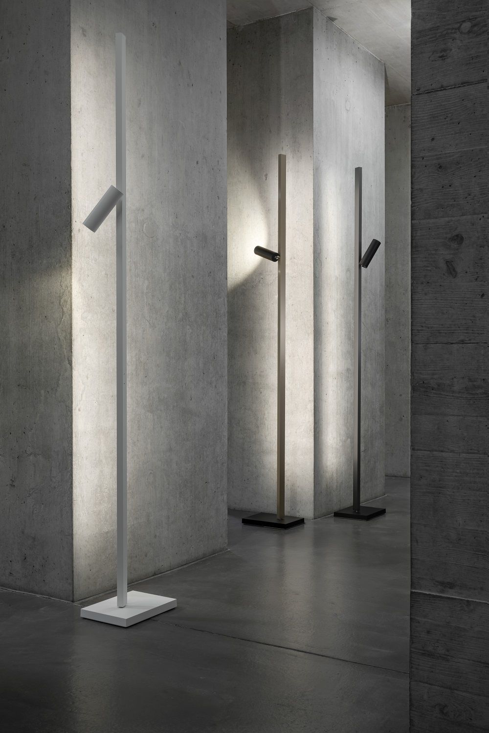 Zen X Floor Stehleuchten in Weiß, Braun und Schwarz vor einer Betonwand.