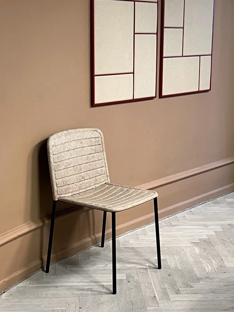 Flax Stacker Chair: Moderner Stuhl mit Leinenstruktur und schwarzen Beinen vor brauner Wand.
