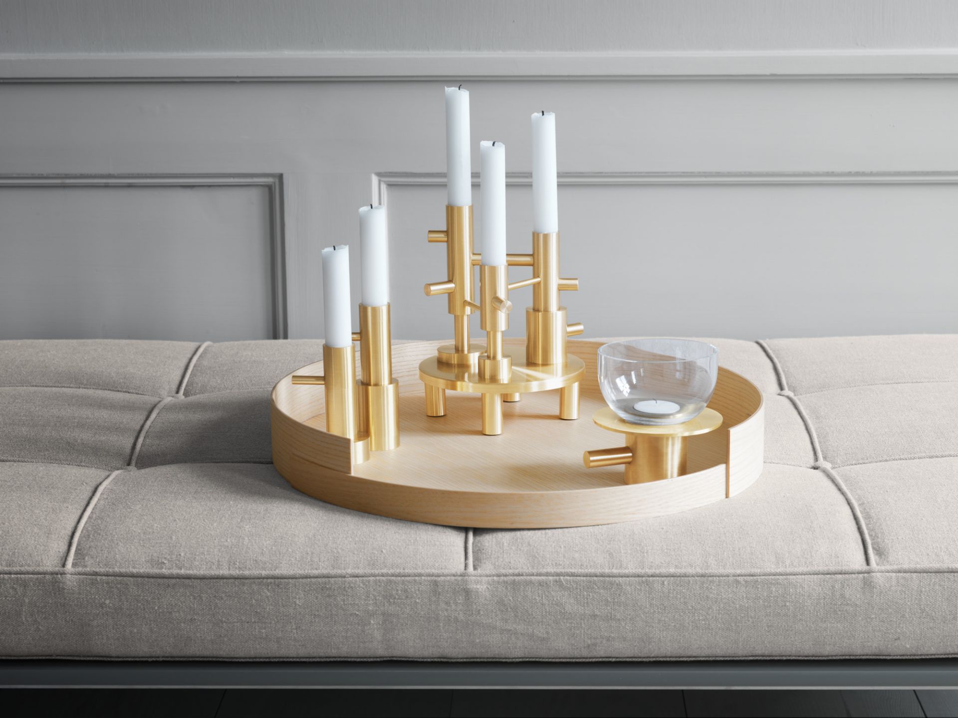 Goldener Fritz Hansen Kerzenhalter mit weißen Kerzen auf Holztablett, dekorative Wohnaccessoires.