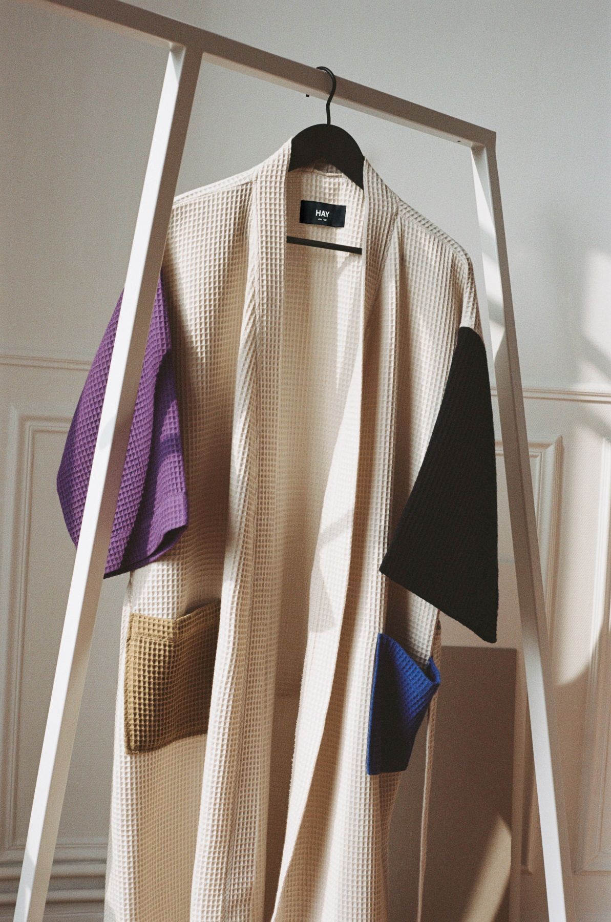 Hay Loop Stand Wardrobe mit beigem Bademantel und farbigen Details an einer weißen Kleiderstange.