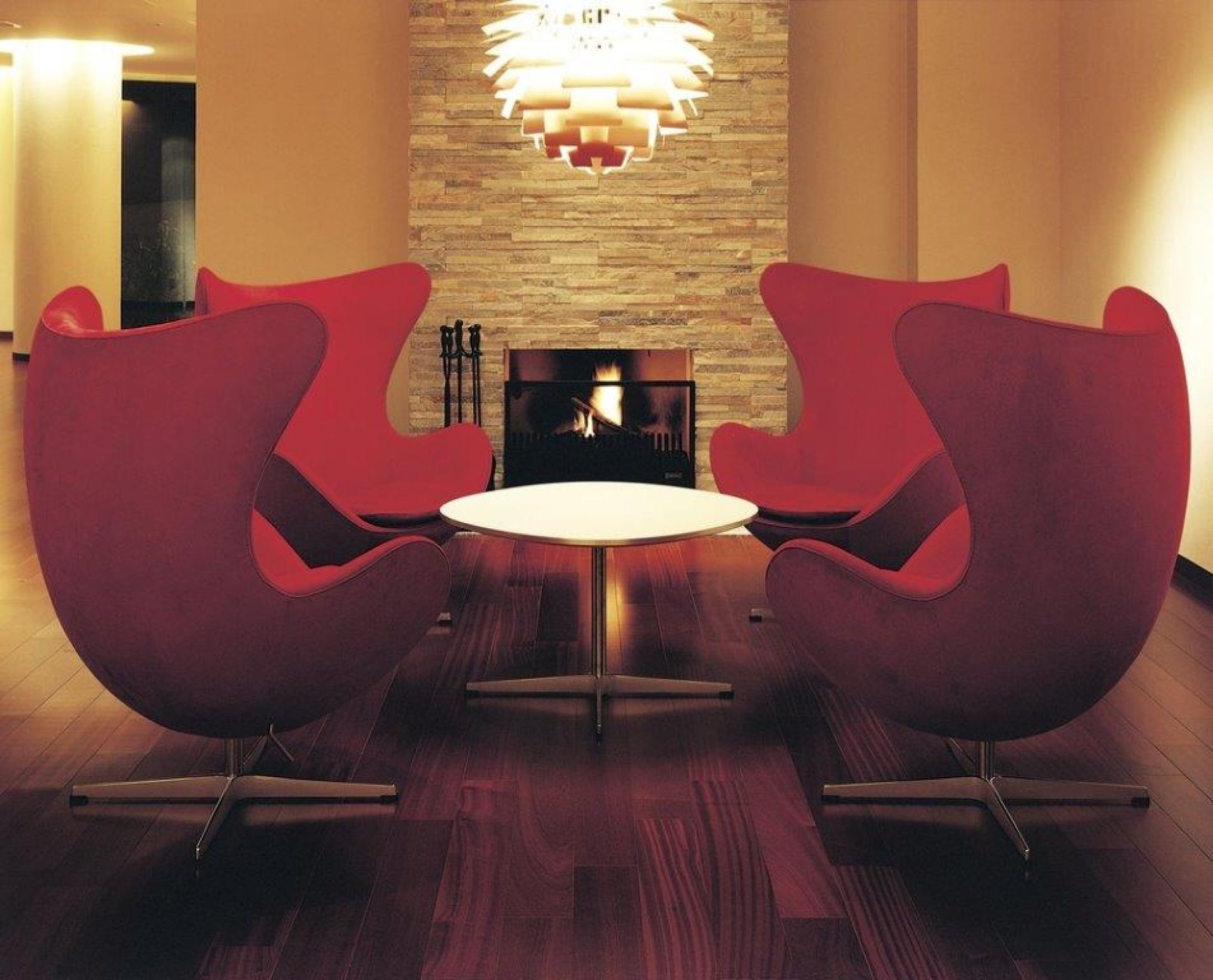 Rote Egg Chairs von Fritz Hansen um einen runden Tisch vor einem Kamin.