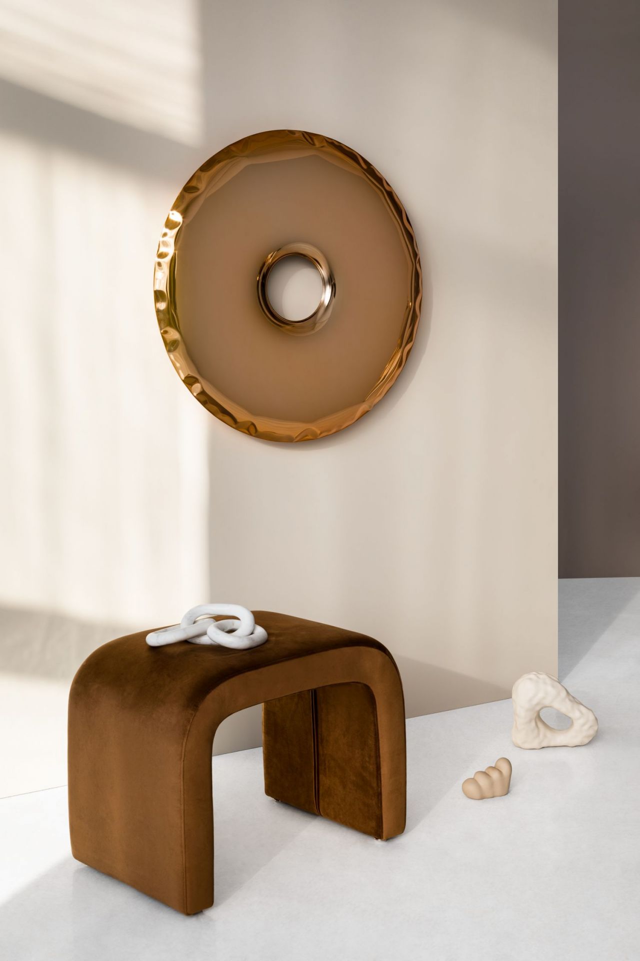 Rondo Spiegel Aurum Gold von Zieta, ein runder Wandspiegel mit goldenem Rahmen über einem braunen Samthocker.