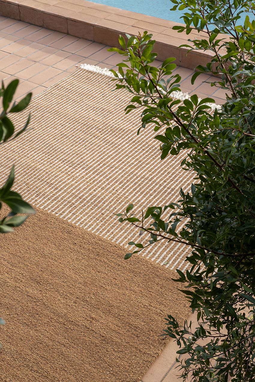 Nanimarquina Garden Outdoor Teppich, braun und beige gestreift, auf einer Terrasse neben einem Pool.