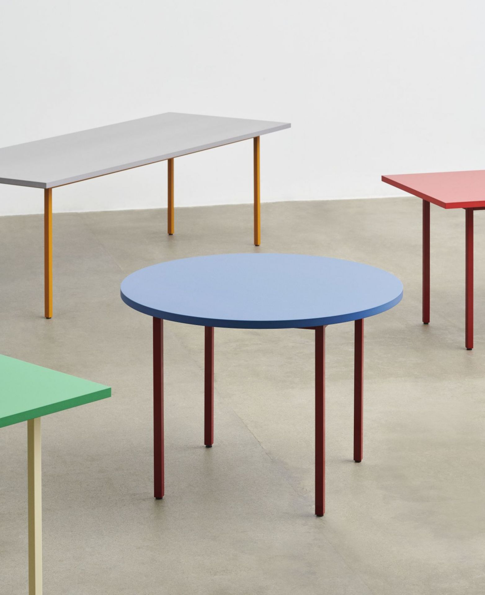 Mehrere farbenfrohe Tische, darunter ein grauer Two Colour Table von Hay mit ockerfarbenem Gestell.