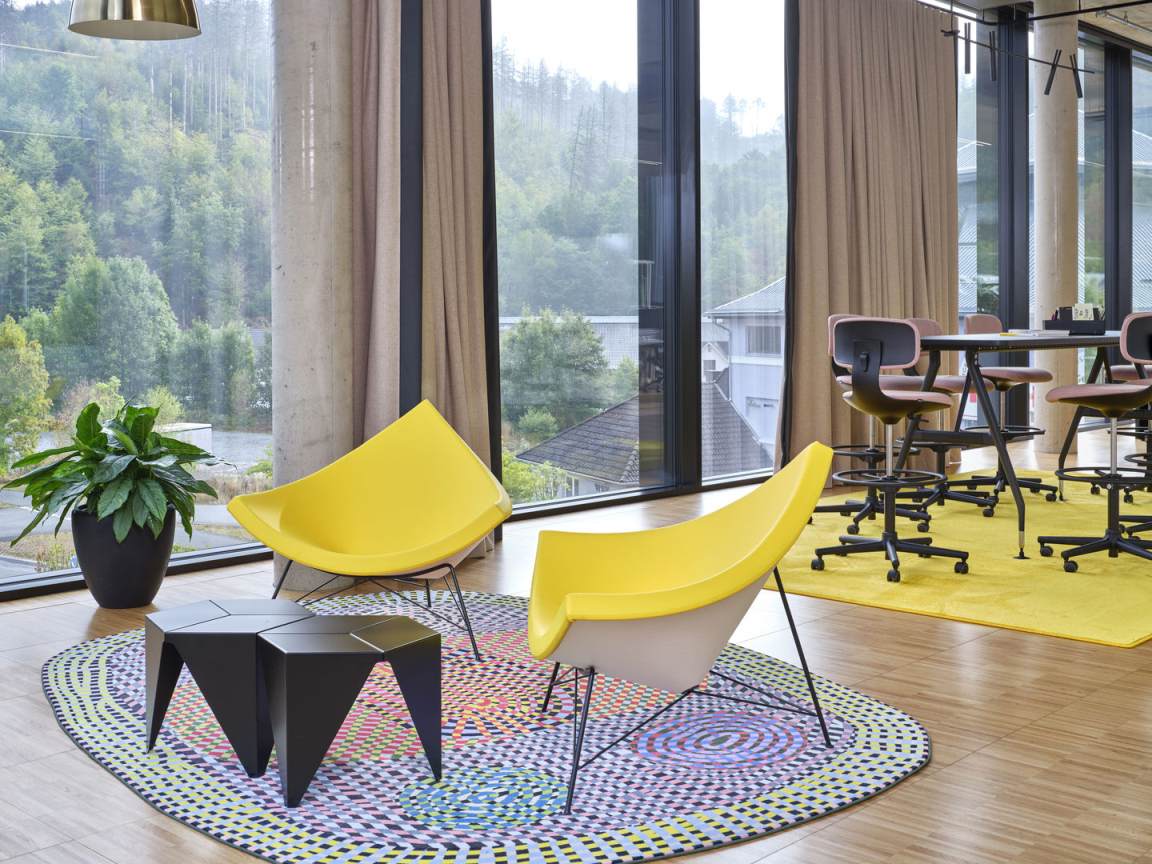 Gelber Vitra Rookie High Bürodrehstuhl in modernem Büroambiente mit Teppich, Tisch und großen Fenstern.