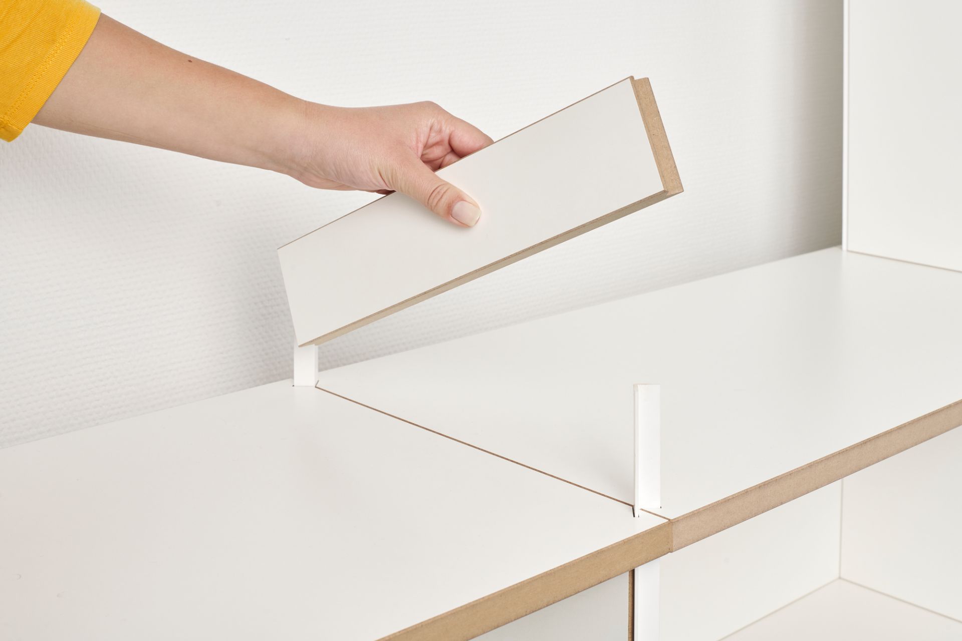 Hand setzt Regalbrett in weißes Tojo Mehrfach Regal Anbaumodul ein. Regalsystem für Wohnzimmer.
