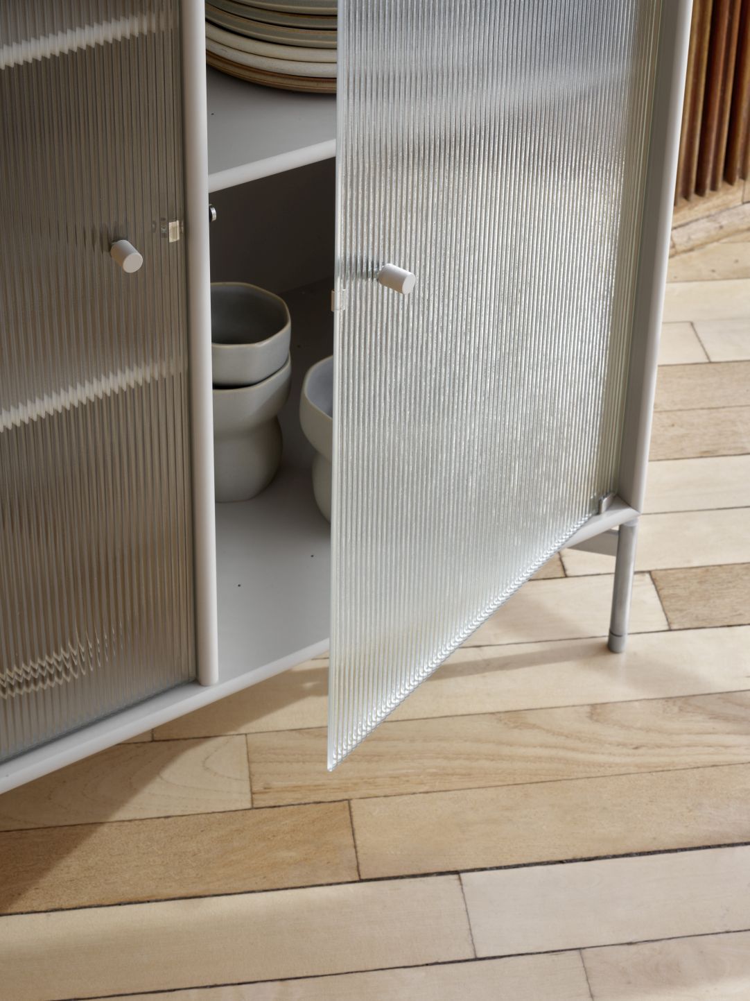 Detailaufnahme: Ripple III Vitrinenschrank mit geriffelten Glastüren und schwarzem Gestell, ideal für moderne Wohnräume.
