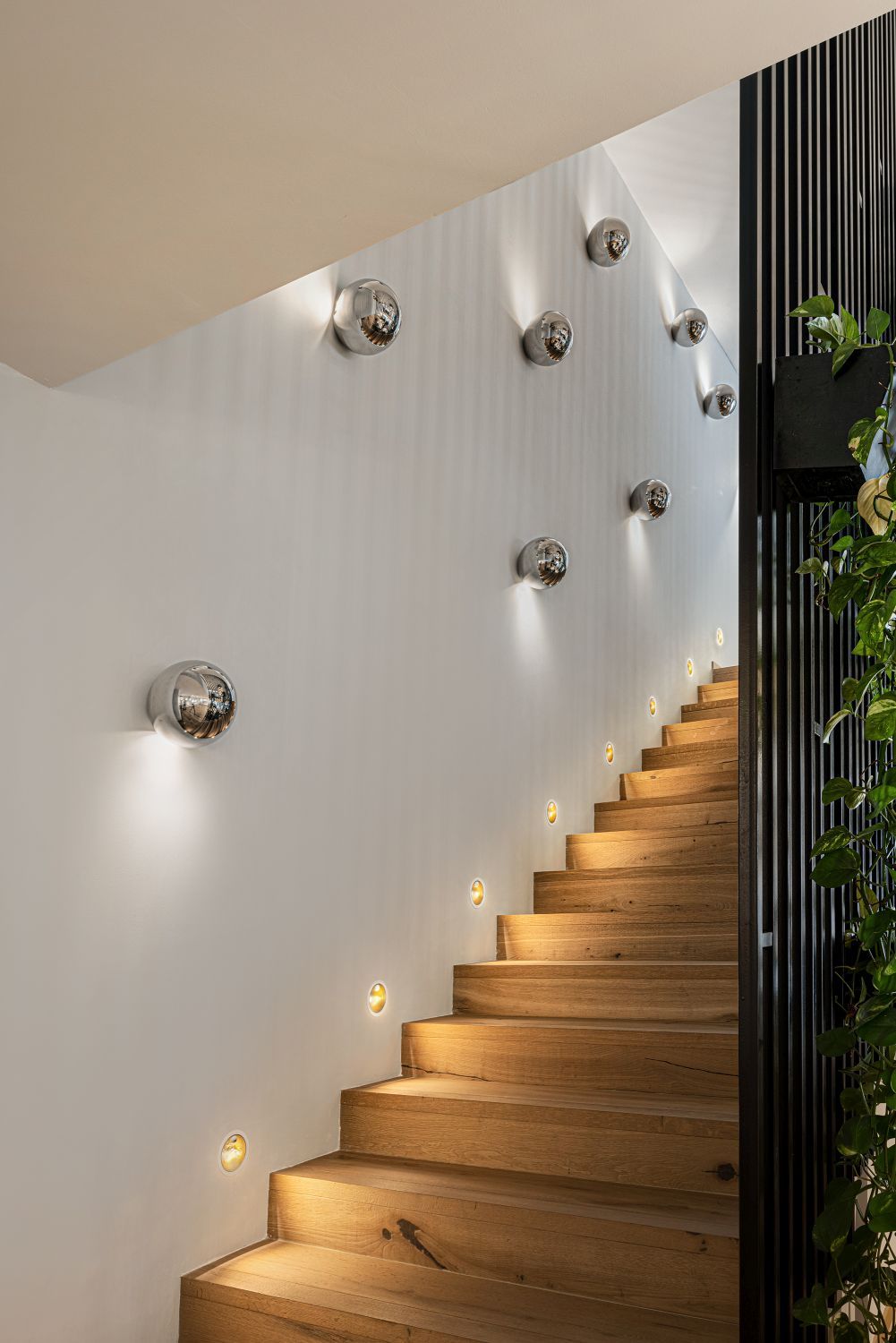 Sfera Wandleuchten von Catellani & Smith beleuchten ein Treppenhaus mit Holzstufen und indirektem Licht.