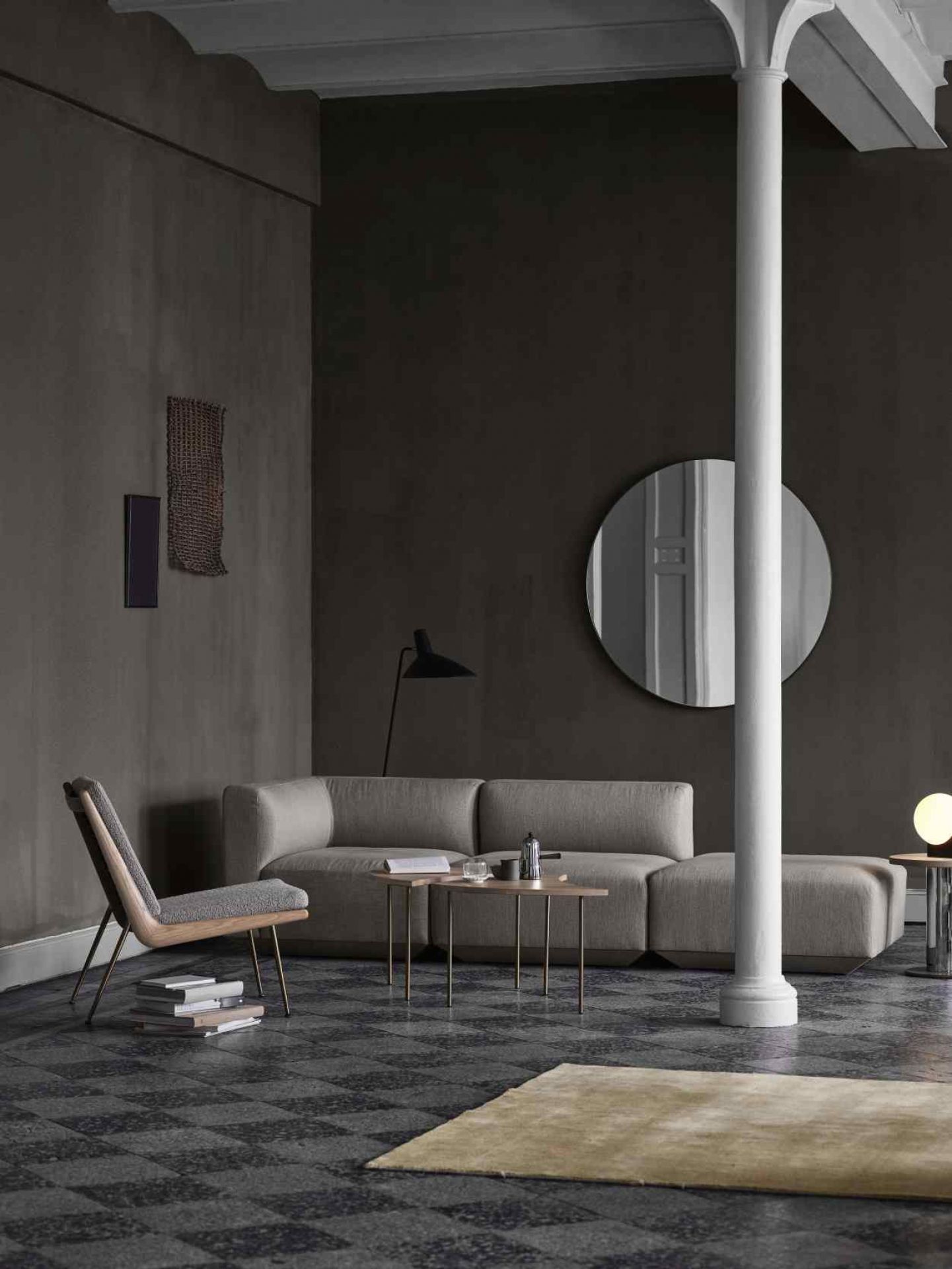 AndTradition Boomerang Lounge Chair HM1 Sessel in grauem Interieur mit Sofa, Tisch und runden Spiegel.