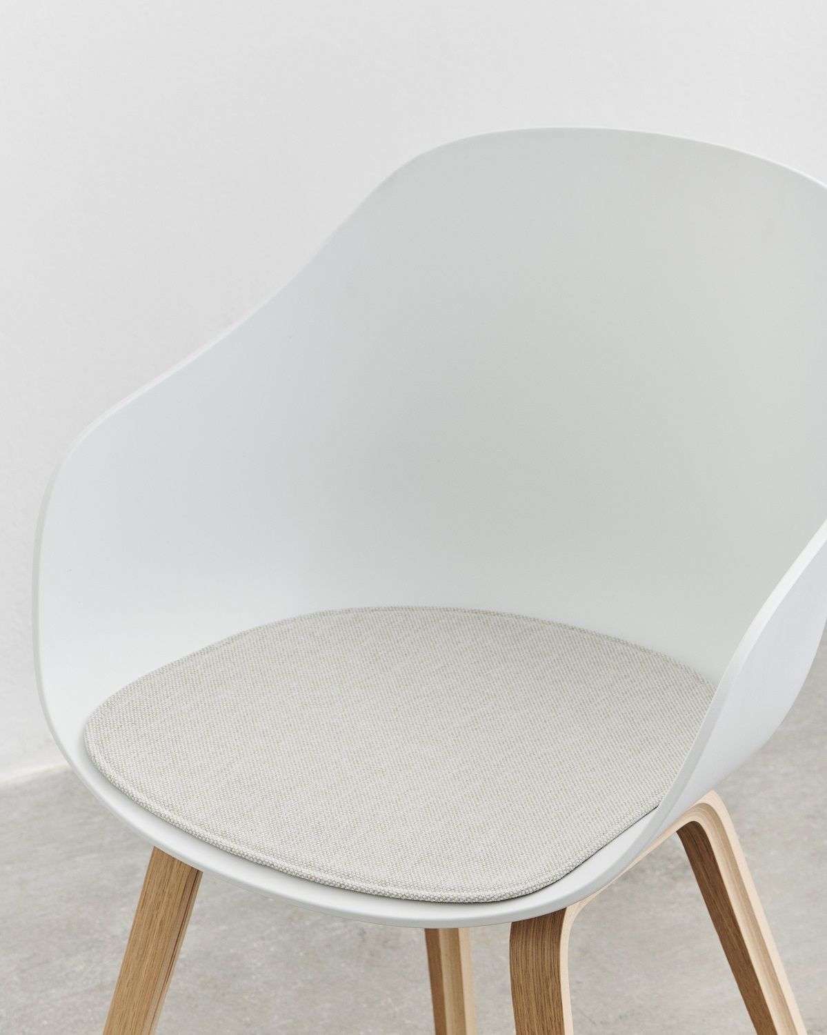 Weißer About A Chair Stuhl mit Armlehnen und grauem Sitzkissen für mehr Komfort.