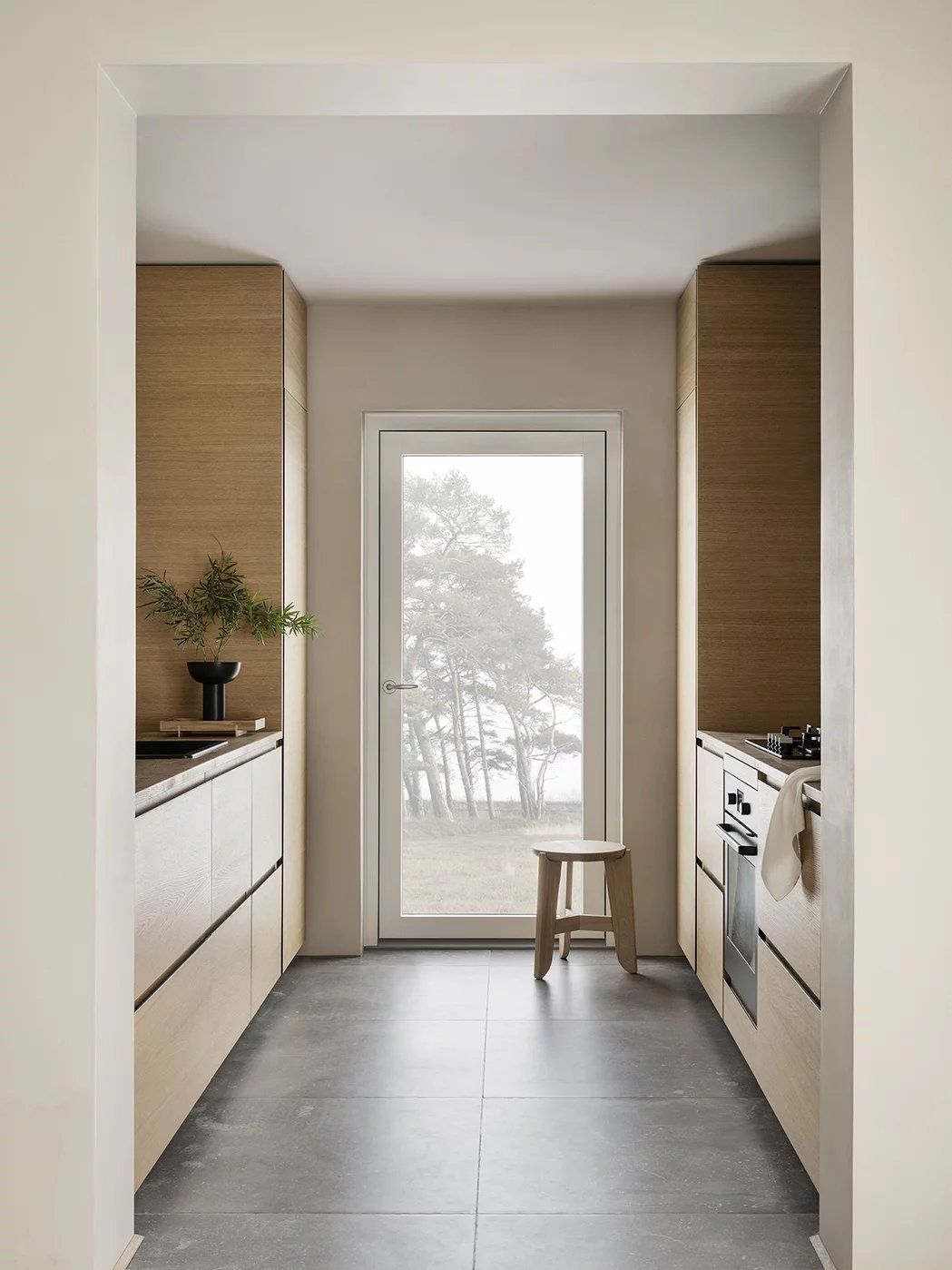 Heller Blomus Eli Hocker aus Holz in minimalistischer Küche mit Holzeinrichtung und Fenster.