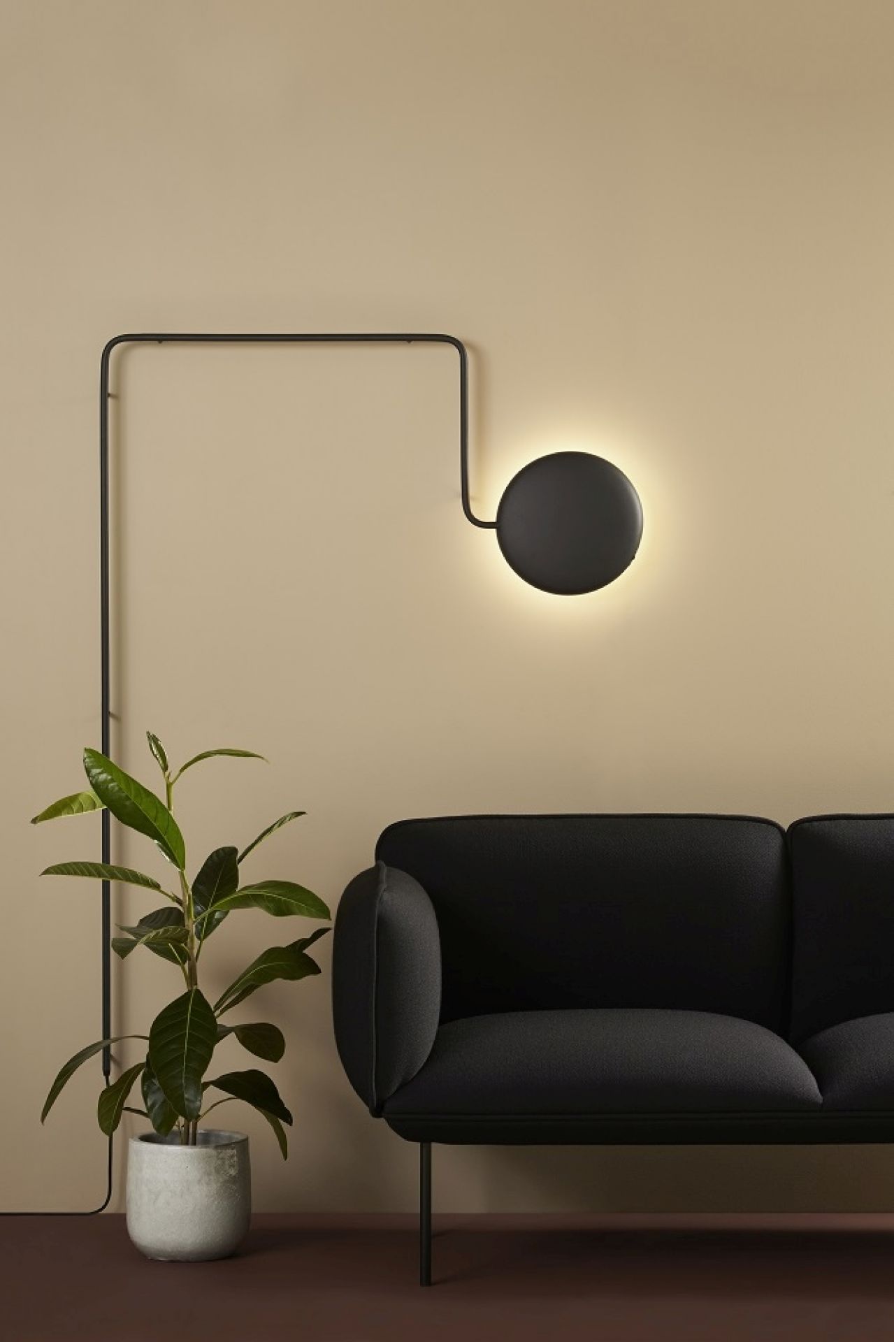 Nakki 2-Sitzer Sofa von Woud in Grau, kombiniert mit moderner Wandleuchte und Zimmerpflanze.