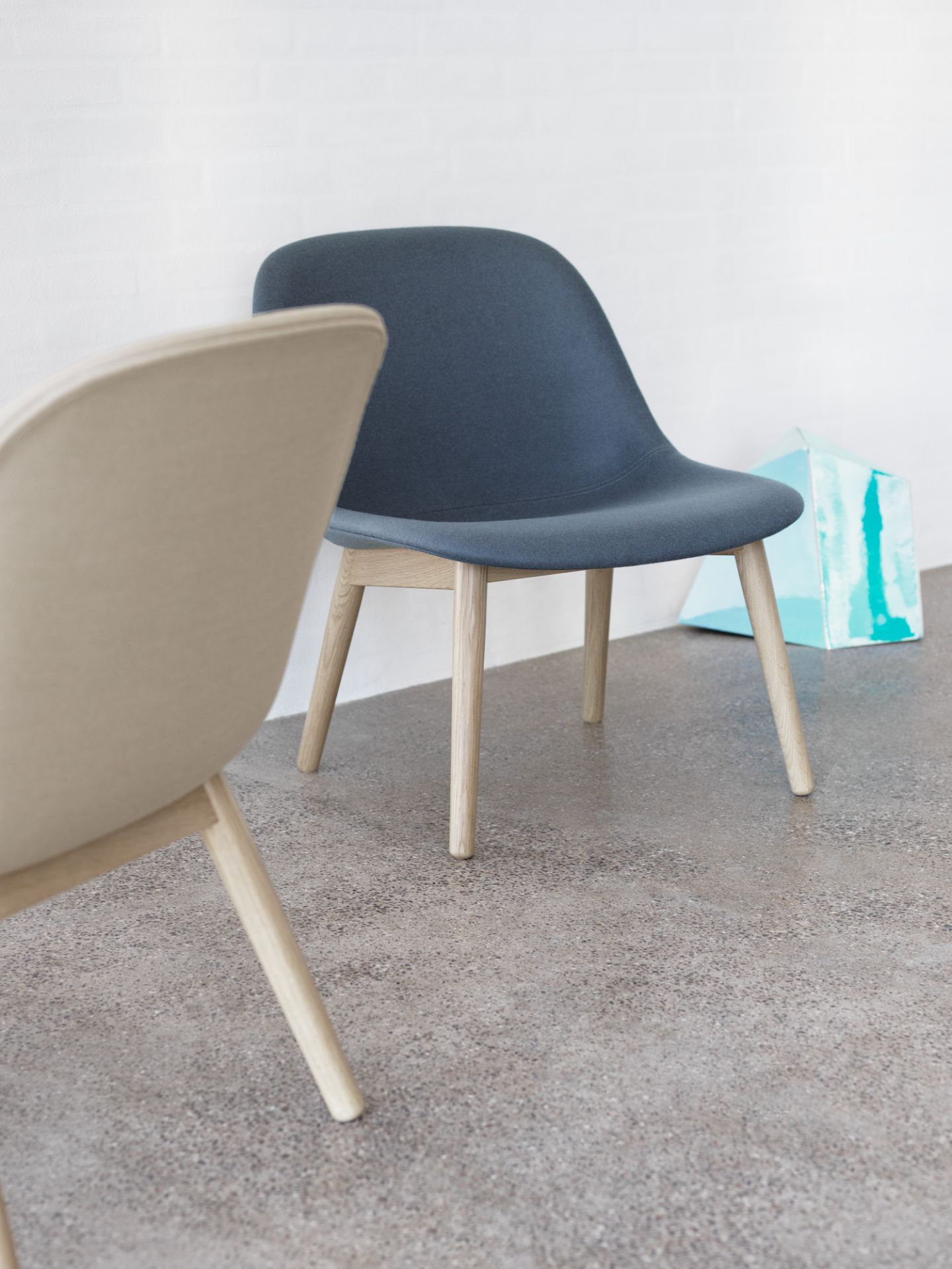 Muuto Fiber Lounge Chair mit Holzgestell in Blau und Beige vor weißer Wand.