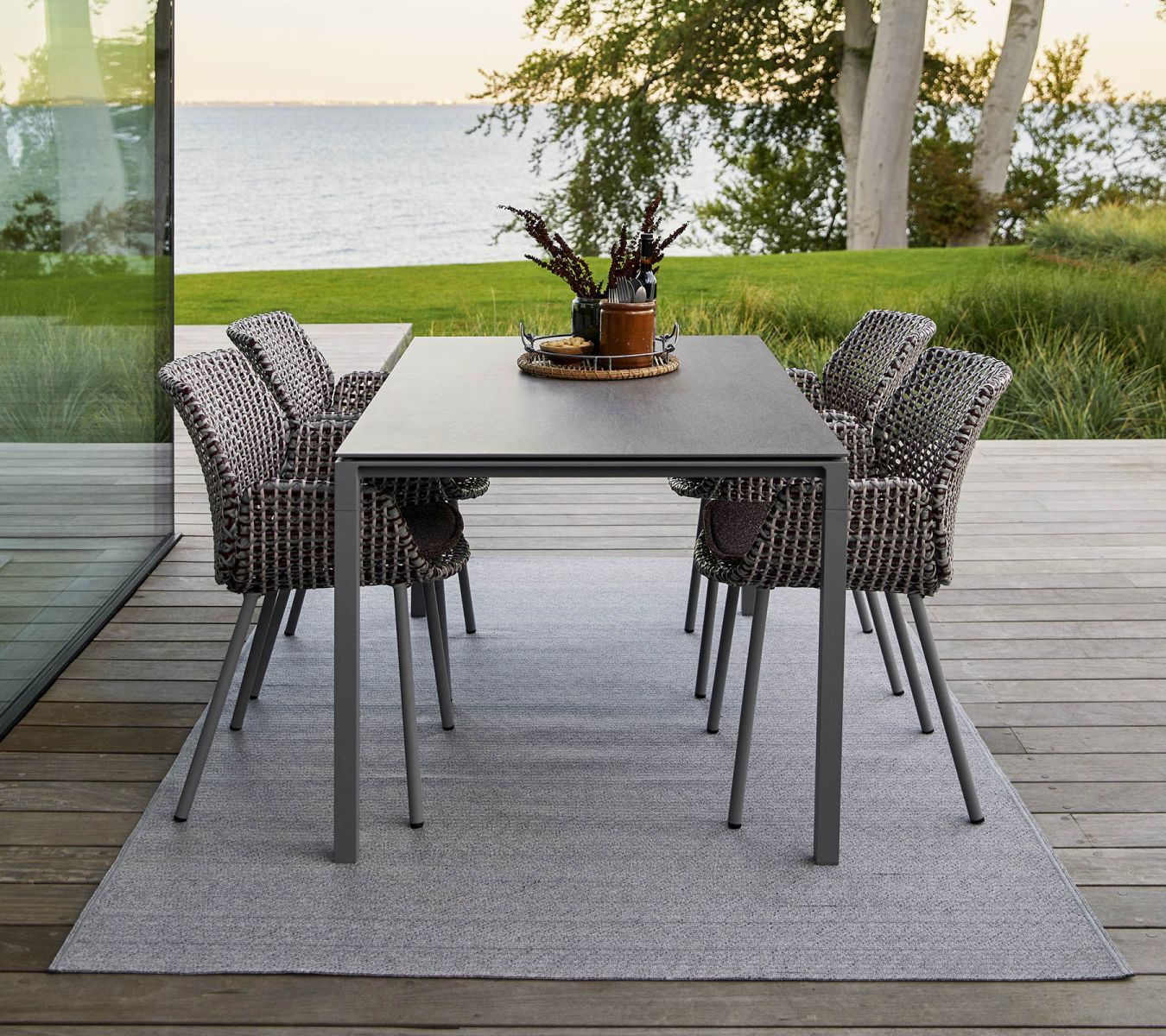 Grauer Dot Outdoor Teppich von Cane-Line (Ø200 cm) unter Esstisch und Stühlen auf Holzterrasse.