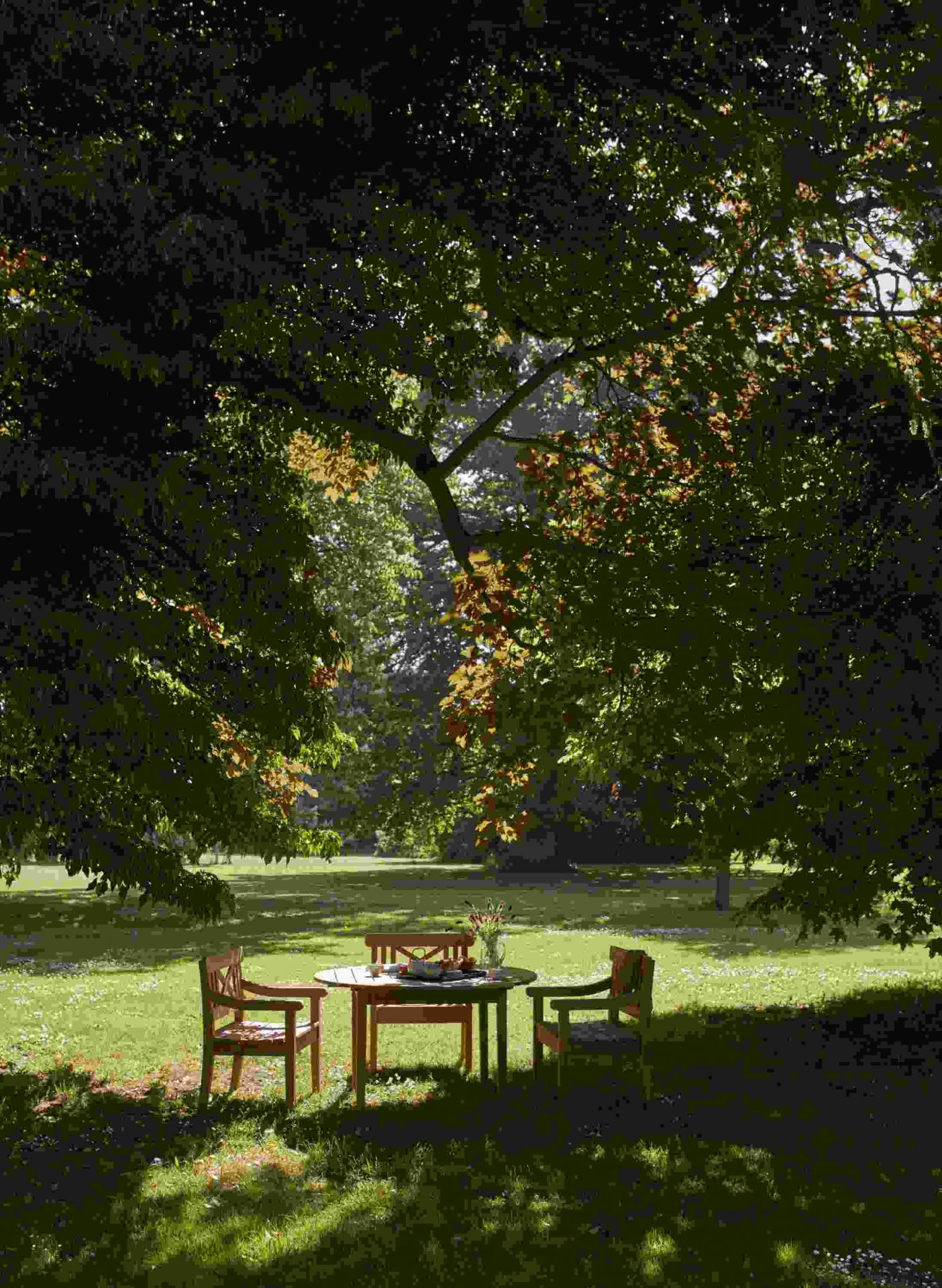 Drachmann Stuhl und Gartentisch von Skagerak by Fritz Hansen unter einem Baum im Garten.