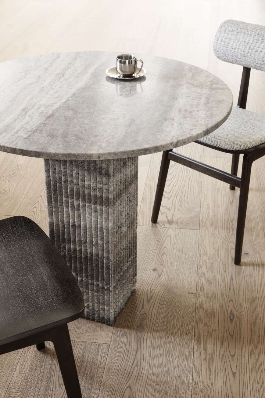 Nahaufnahme des NORR11 Totem Chair Stuhls mit grauem Polster und passendem Esstisch aus Travertin.