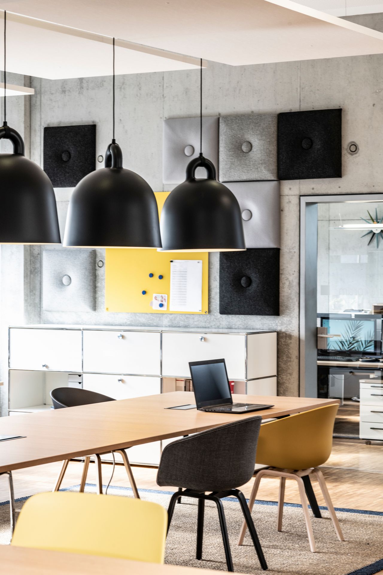 Drei schwarze Bell Lamp Hängeleuchten von Normann Copenhagen über einem modernen Konferenztisch in einem Büro.