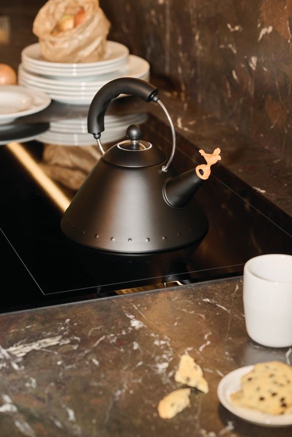 Schwarzer 9093 BB Wasserkessel von Alessi auf einem Induktionskochfeld mit Vogelpfeife und Teetasse.